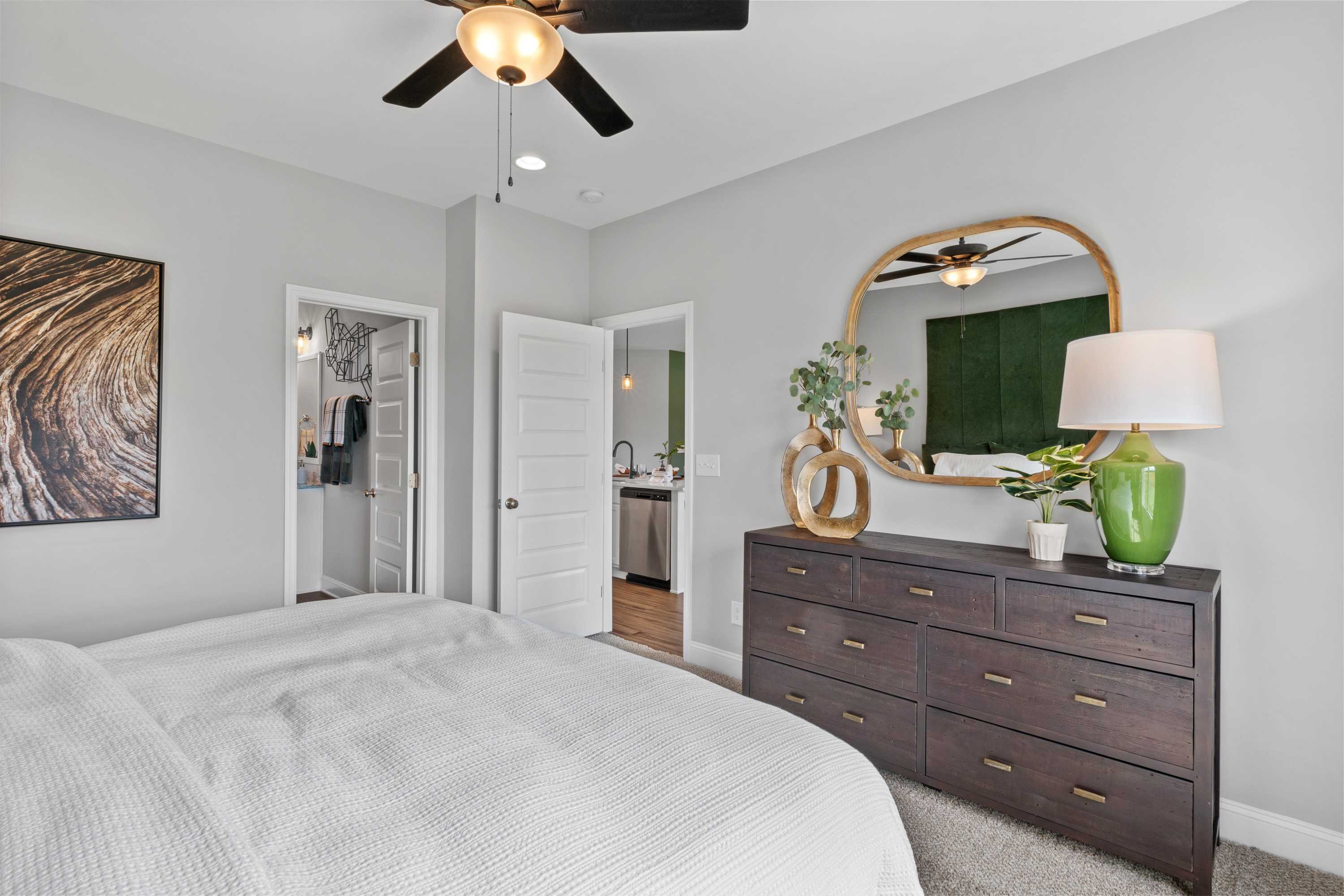 Spacious master bedroom at Wood Trail in Toney Alabama with king bed, dark wood dresser, gold mirror, green accents and open en-suite bath