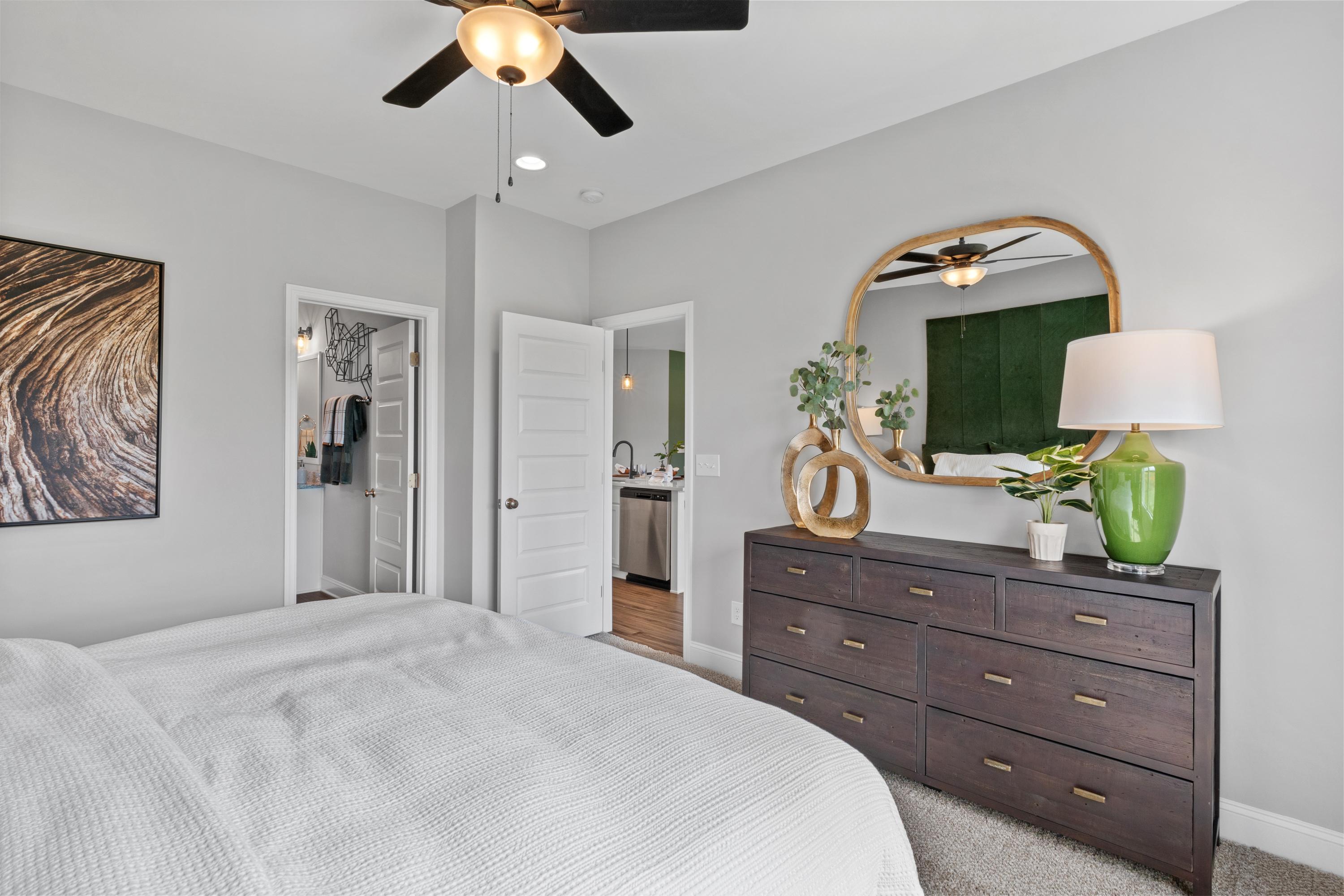 Spacious master bedroom at Wood Trail in Toney Alabama with king bed, dark wood dresser, gold mirror, green accents and open en-suite bath