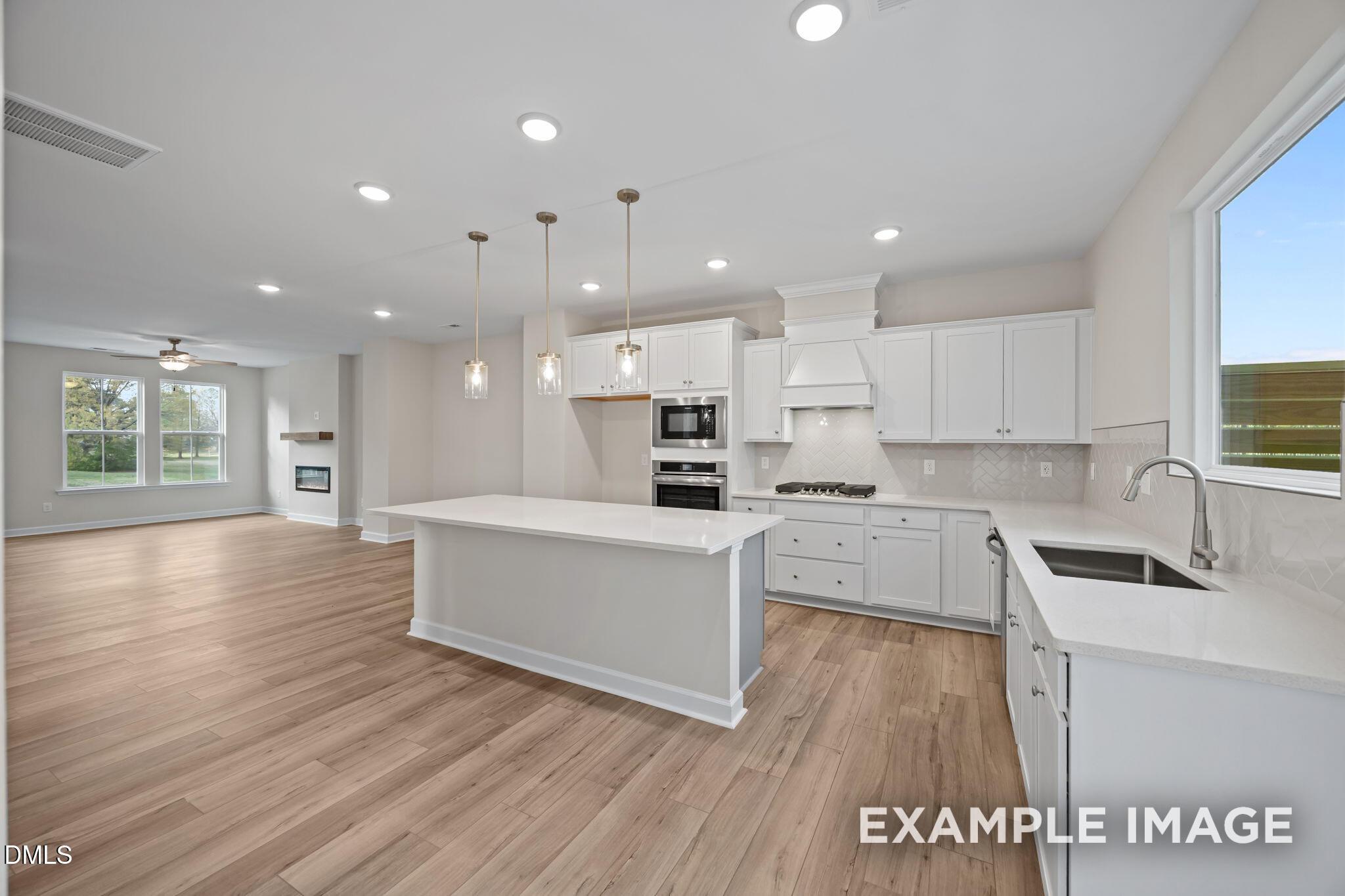 Open-concept kitchen with white shaker cabinets, quartz island, stainless appliances, and living room fireplace in Davidson Homes The Avery, Knightdale, NC