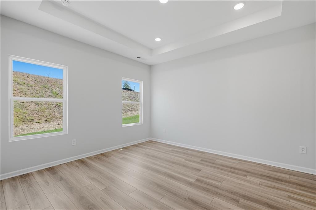 Bright bedroom with hardwood-style flooring, tray ceiling, and dual windows in Davidson Homes' The Oconee B, The Bluffs, Canton, GA