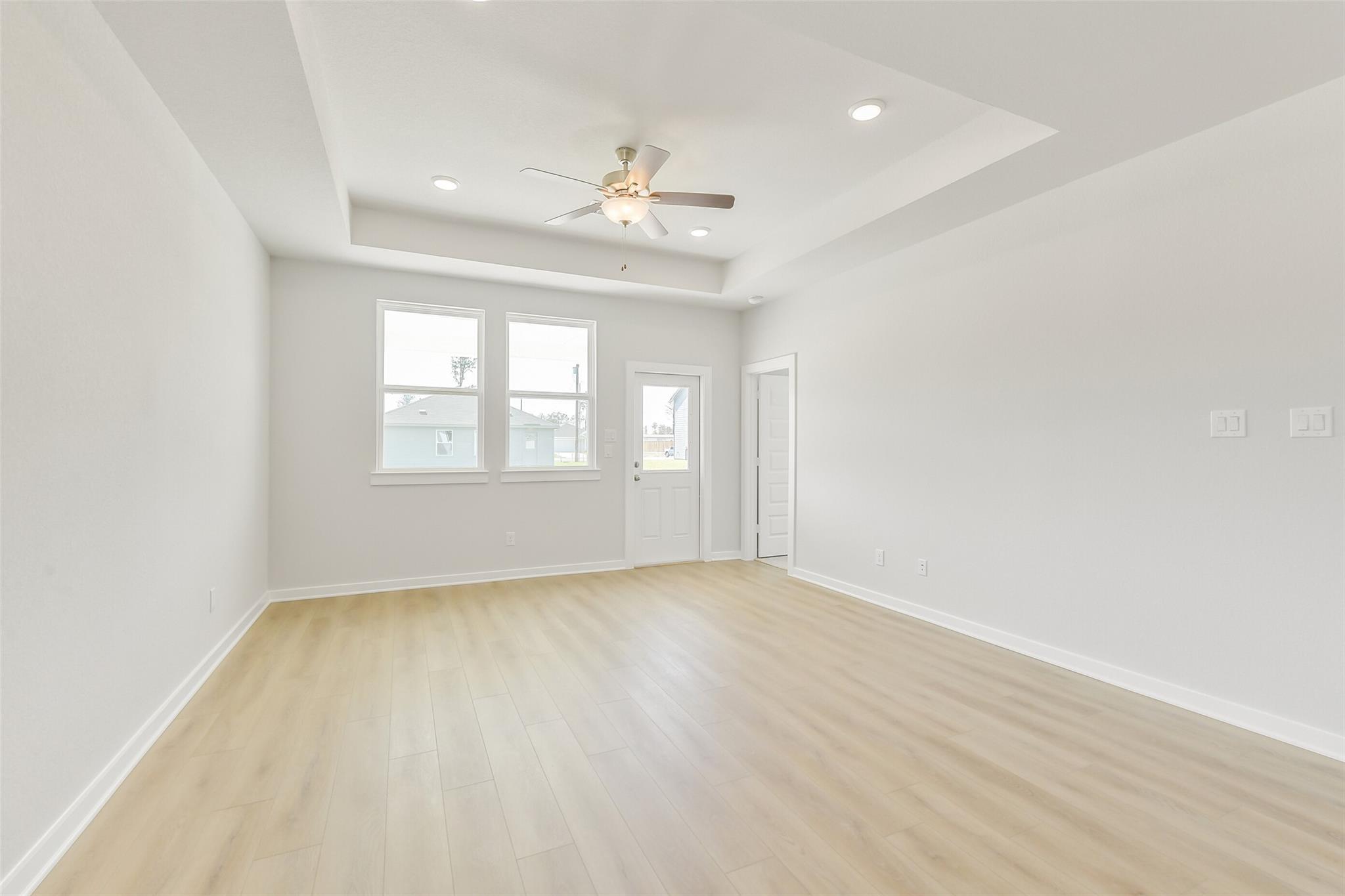 Bright living room with tray ceiling, ceiling fan, large windows, French doors, and light oak floors in Davidson Homes The Frio G, Conroe Texas