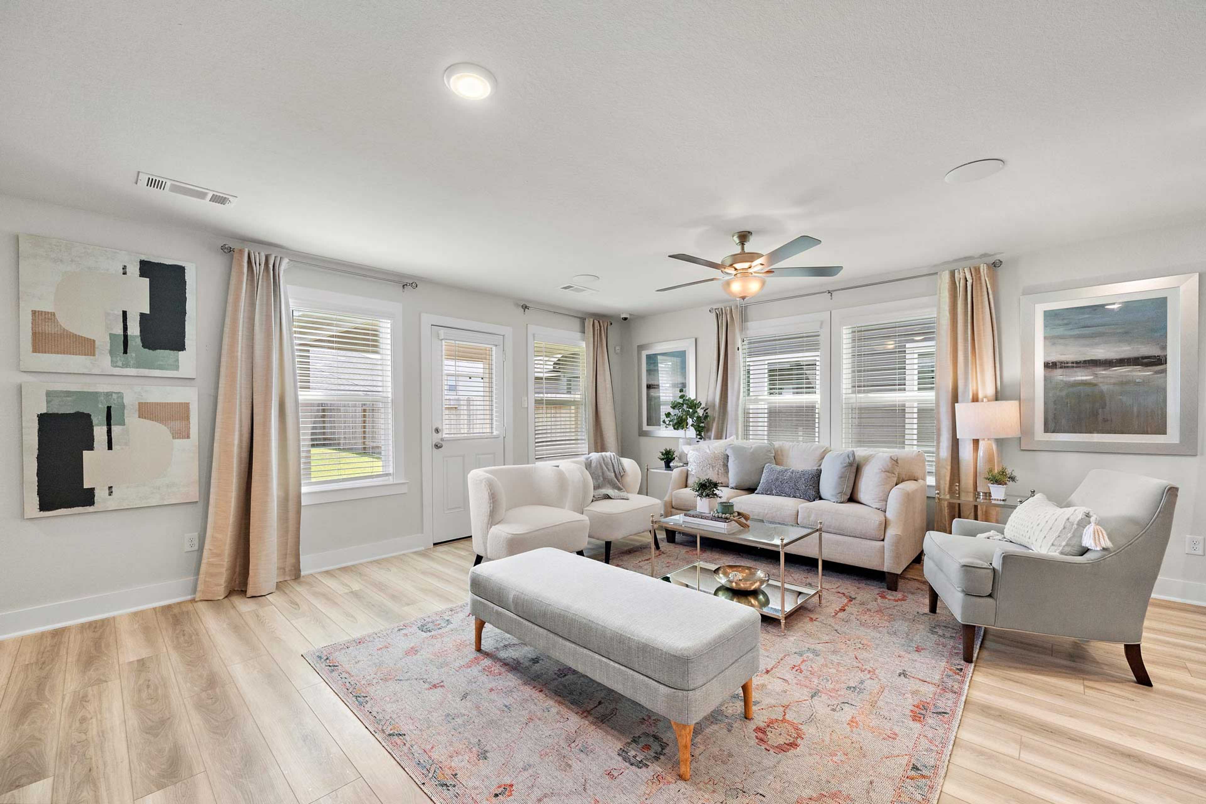 Spacious living room at Haven at Kieth Harrow in Cypress Texas with beige sofas hardwood floors large windows and abstract art