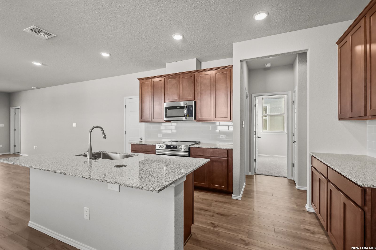 Modern open-concept kitchen with granite island, stainless appliances, and wood cabinets in The Frio B home, San Antonio, Texas