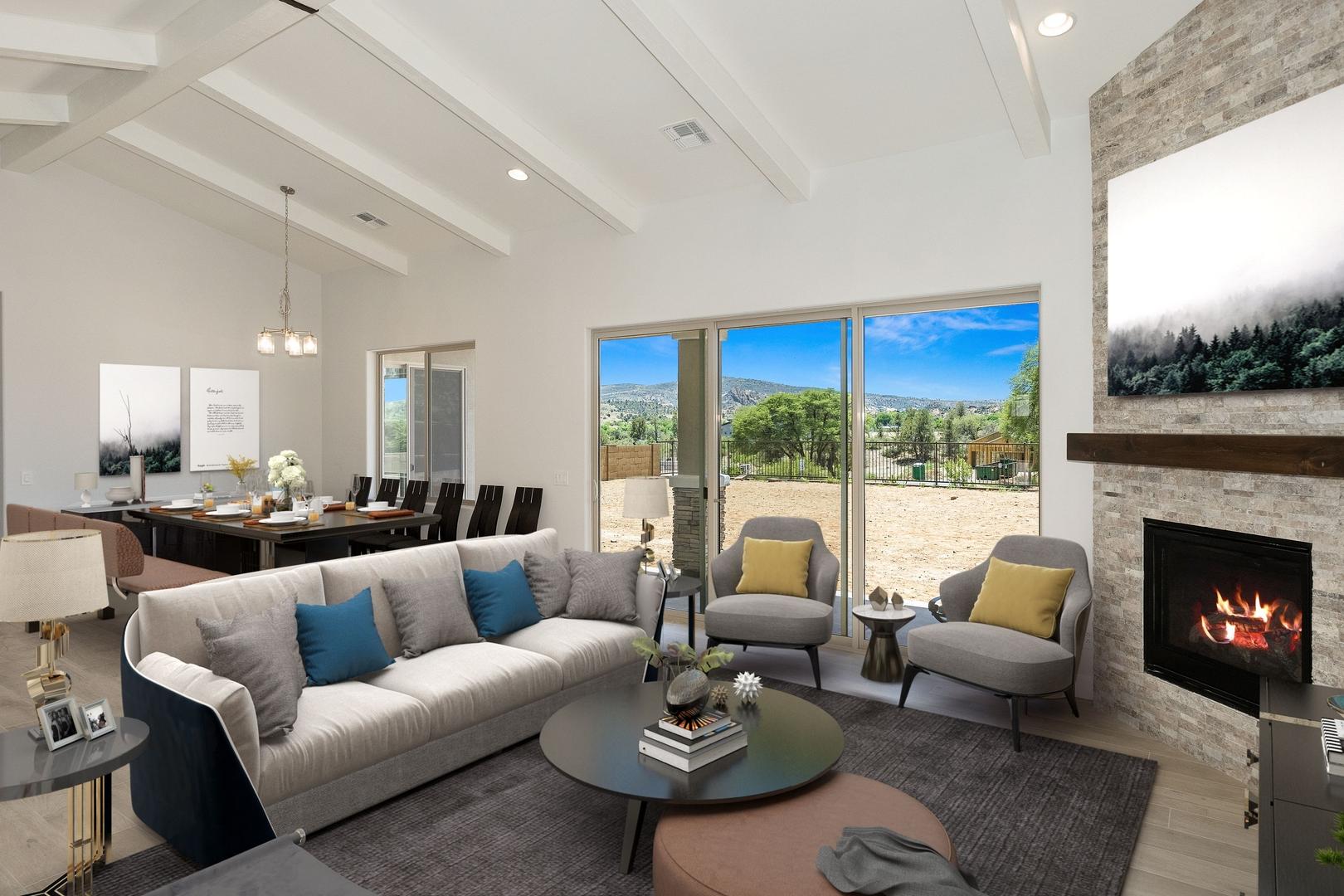 Spacious open-concept living room in The Daybreak E with vaulted ceilings, stone fireplace, gray sofas, and desert view windows