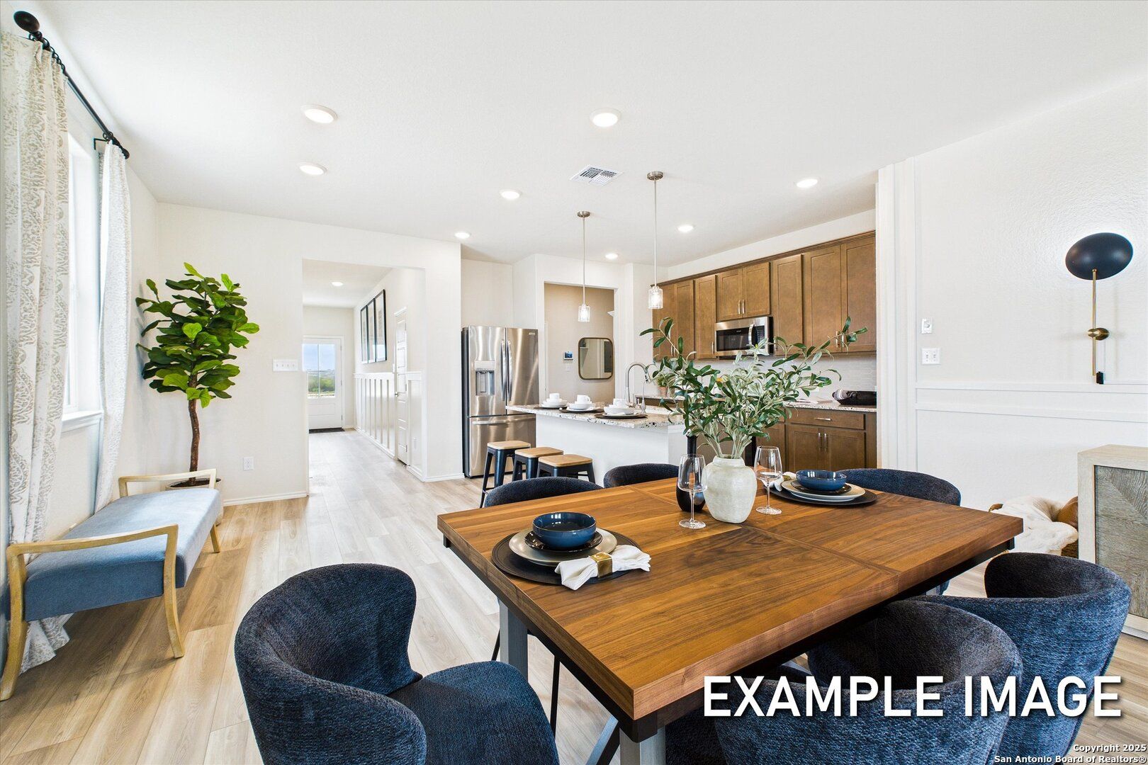 Modern open-concept dining room with wooden table, blue chairs, and adjacent kitchen in Davidson Homes The Brazos C, San Antonio