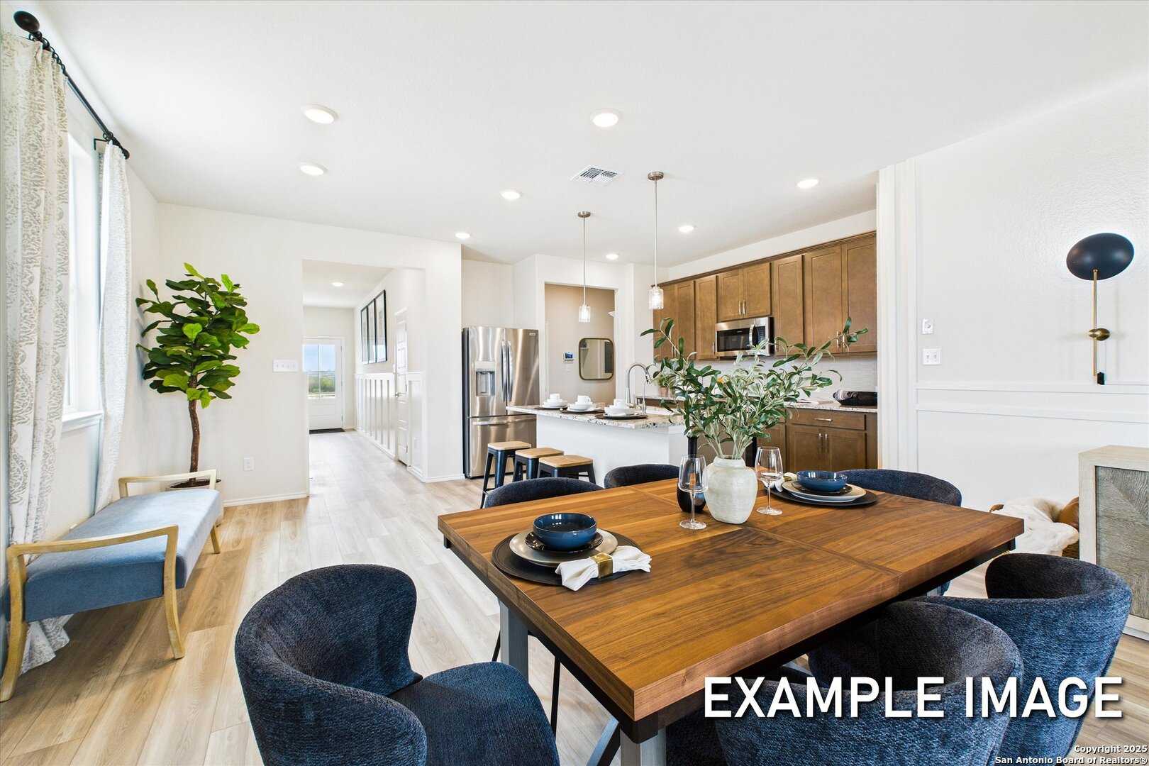 Open-concept dining room with wooden table, blue velvet chairs, and adjacent kitchen featuring oak cabinets and stainless appliances in 5-bedroom San Antonio home