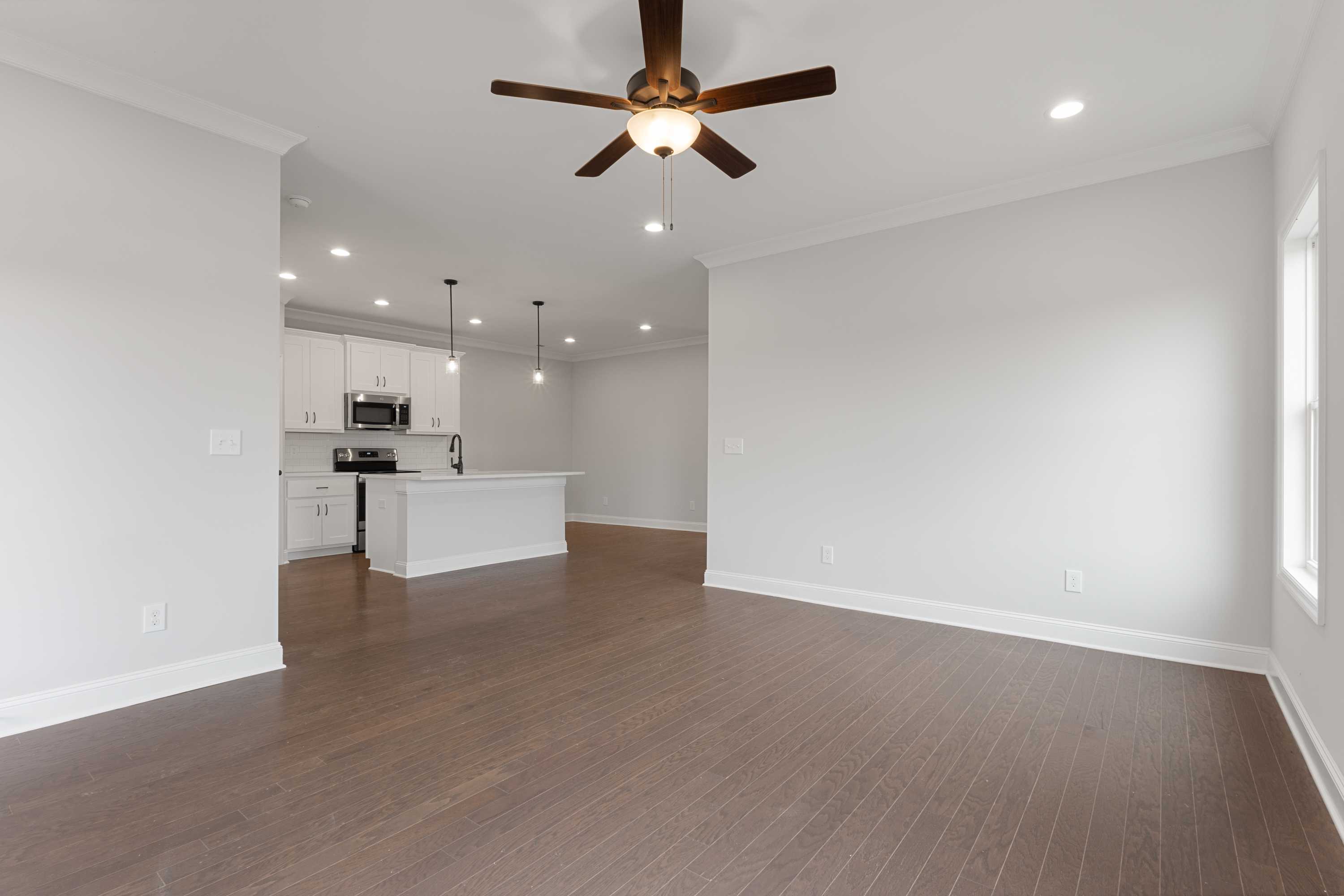 Open-concept kitchen-living area in The Copeland home by Davidson Homes, white cabinets, large island, hardwood floors, ceiling fan