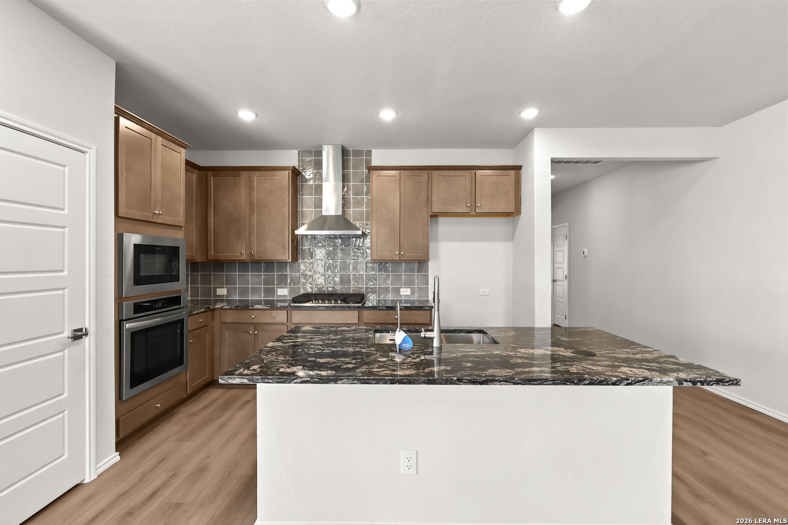 Modern kitchen with granite island, stainless appliances, and wood-tone cabinets in Davidson Homes' Daphne I plan, San Antonio