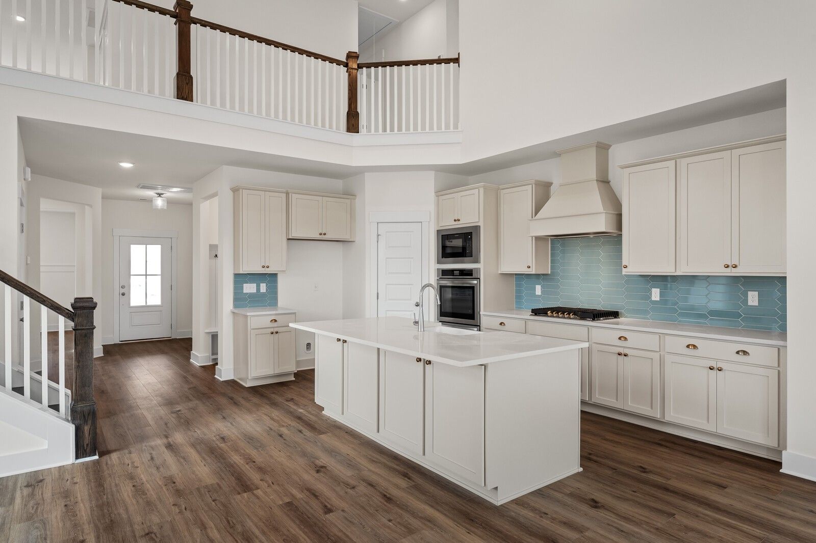 Open-concept kitchen featuring white shaker cabinets, blue glass backsplash, stainless appliances, and large island in Davidson Homes The Ridgeport, Gallatin, TN