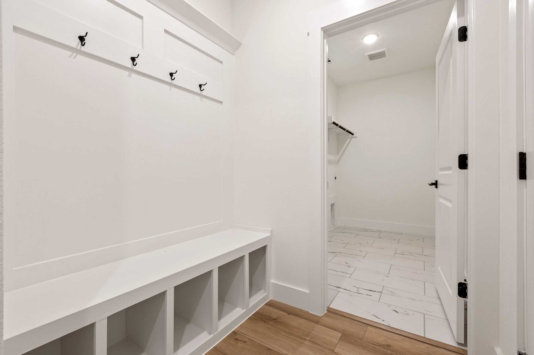 Functional mudroom with white built-in bench, coat hooks, and laundry room access in Davidson Homes The Rockford C, Josephine, Texas