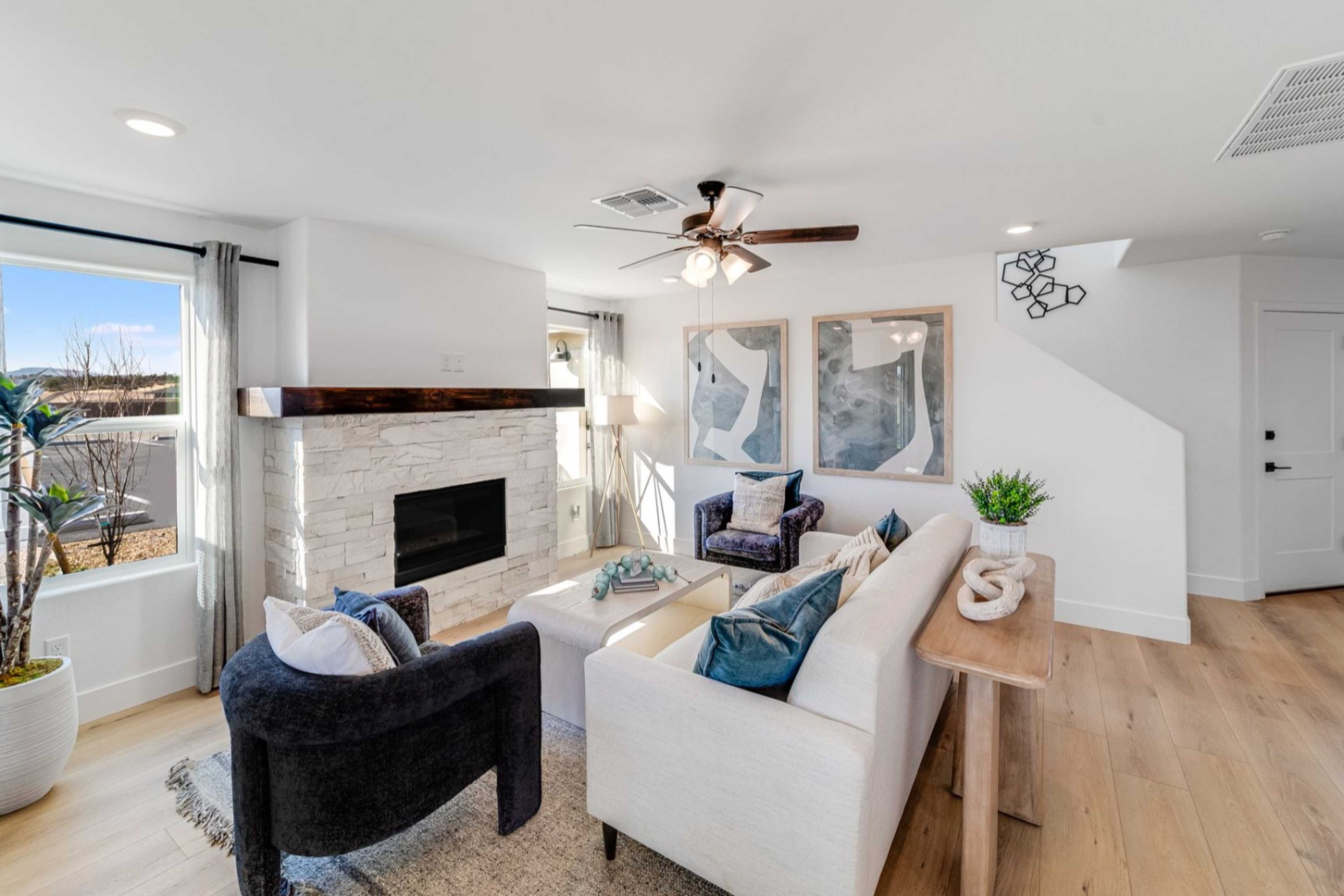 Cozy living room in The Wilmington B featuring stone fireplace, blue sectional sofa, ceiling fan, and Prescott desert views