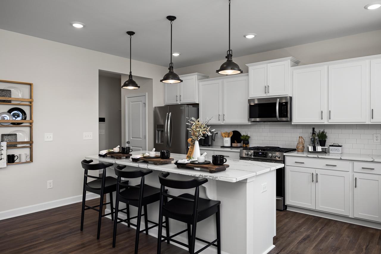 Spacious white kitchen in Wellers Knoll, Lillington NC with island, black stools, stainless appliances, hardwood floors by Davidson Homes