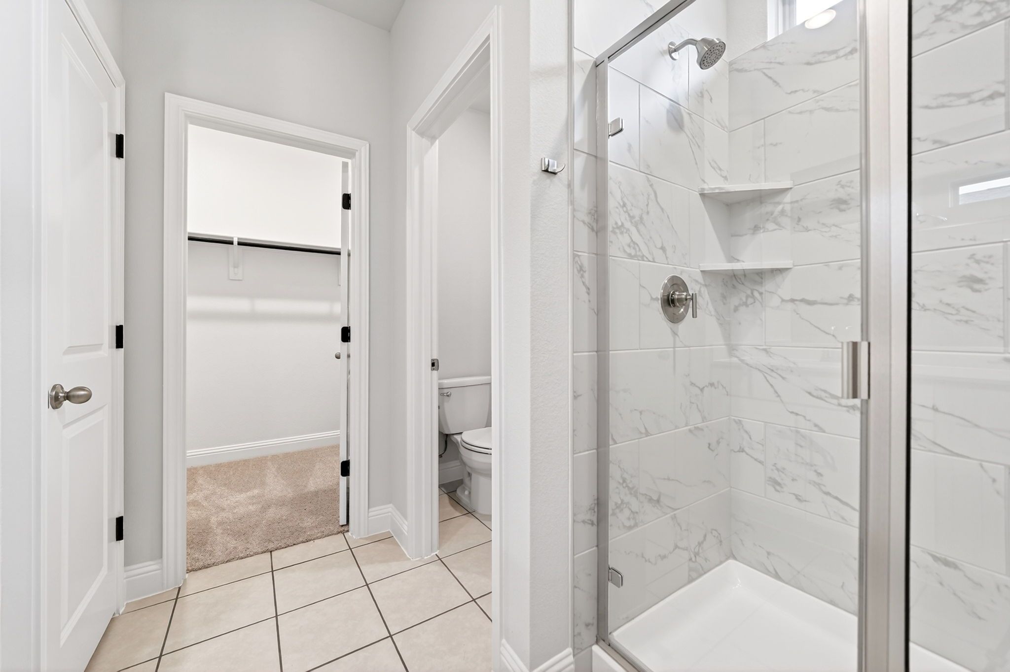 Master suite bathroom in The Redbud featuring a walk-in shower with marble-look tile, private water closet, and closet.