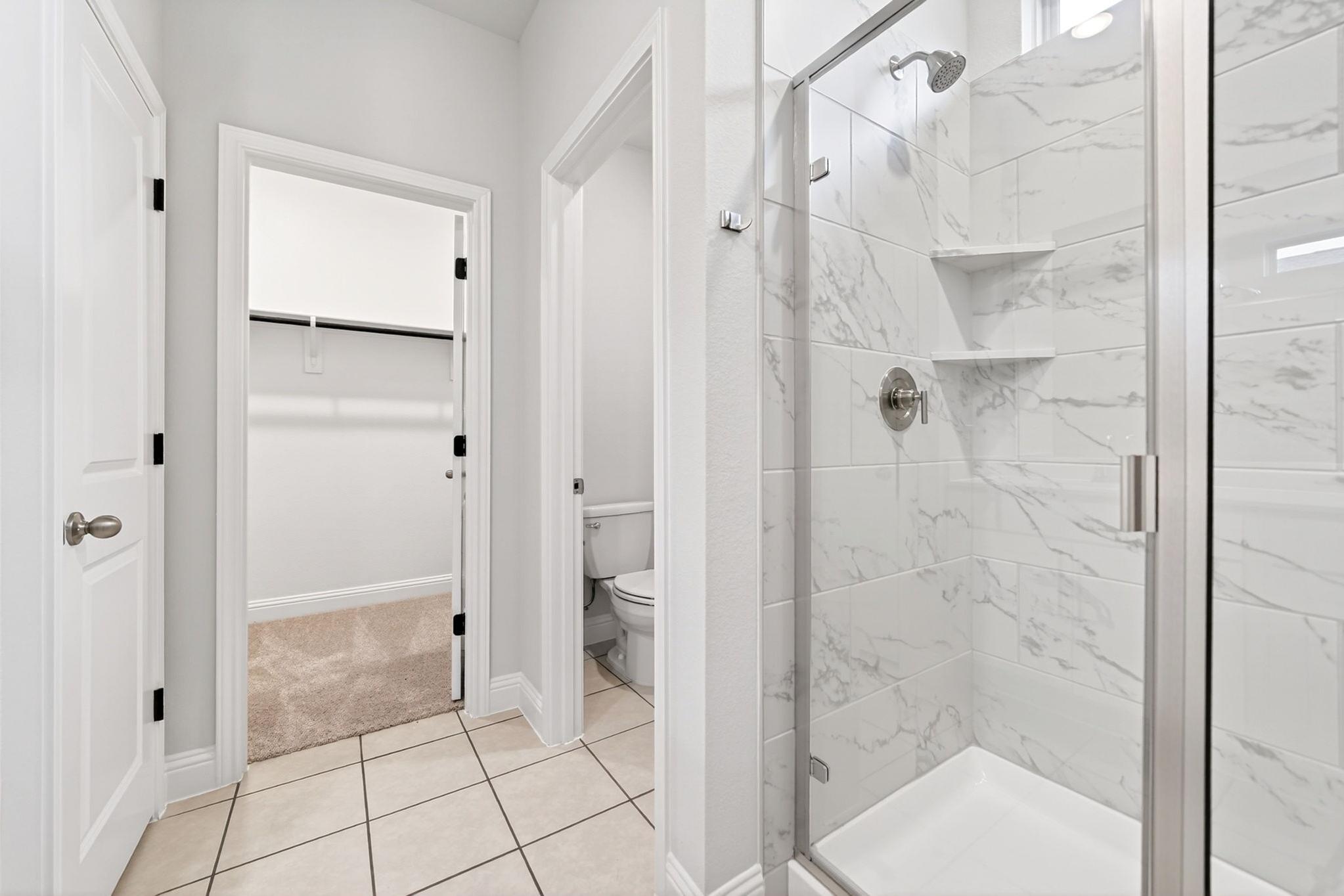 Master suite bathroom in The Redbud featuring a walk-in shower with marble-look tile, private water closet, and closet.