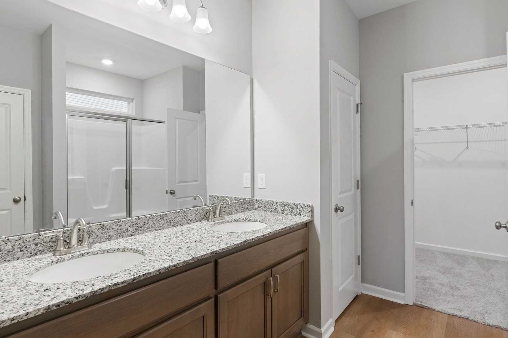 Modern master bathroom in The Luna featuring double granite vanity, walk-in shower, and open closet door