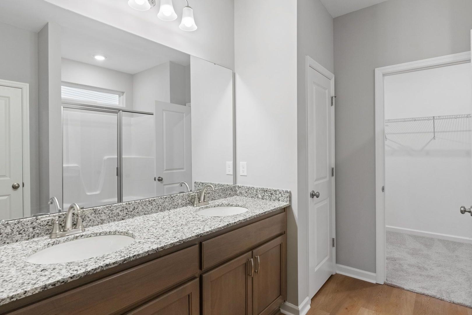 Modern master bathroom in The Luna featuring double granite vanity, walk-in shower, and open closet door