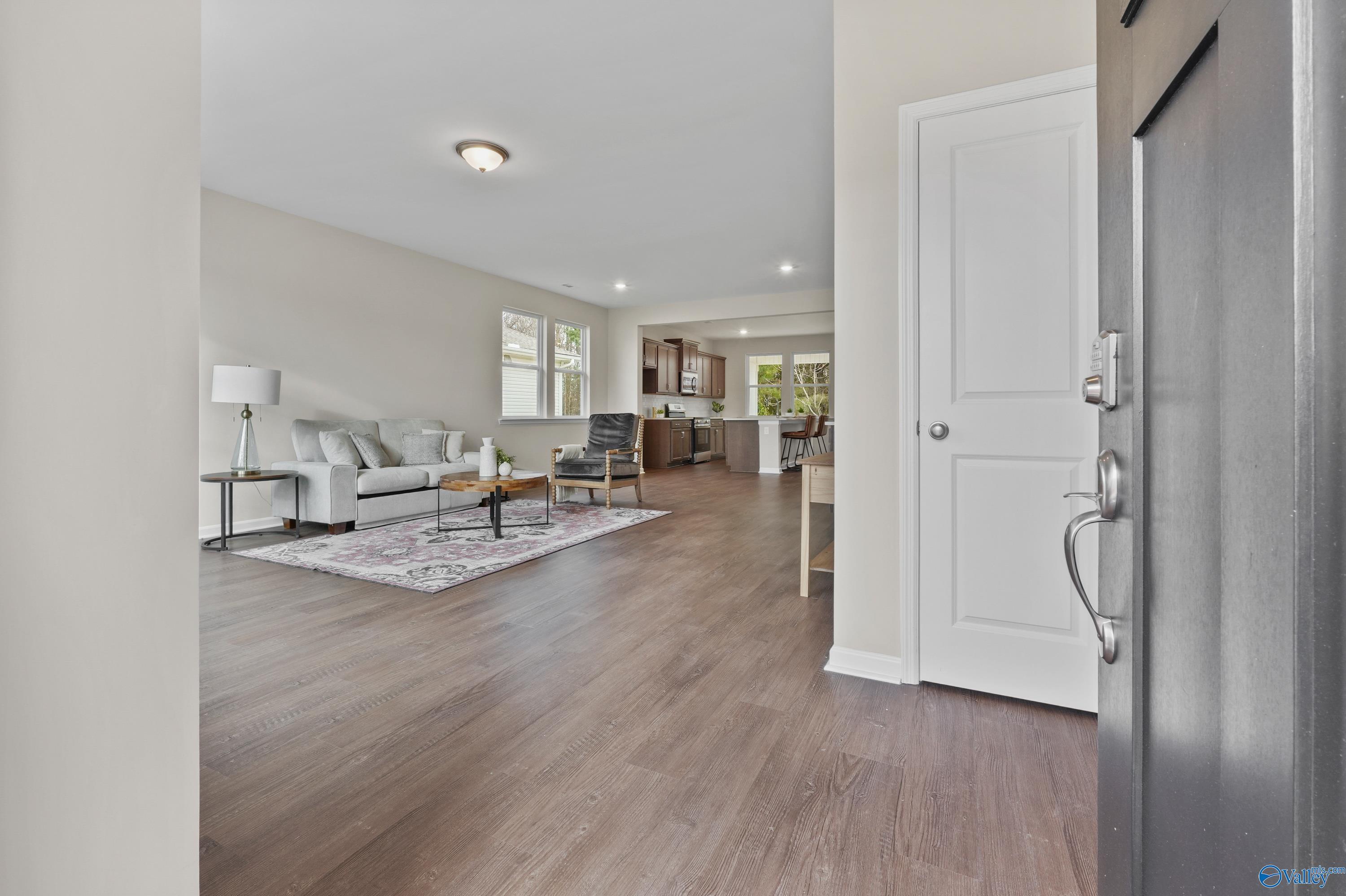 Open-concept living room with beige sofa, hardwood floors, and kitchen view from entry in The Stella 3-bedroom home, Hazel Green