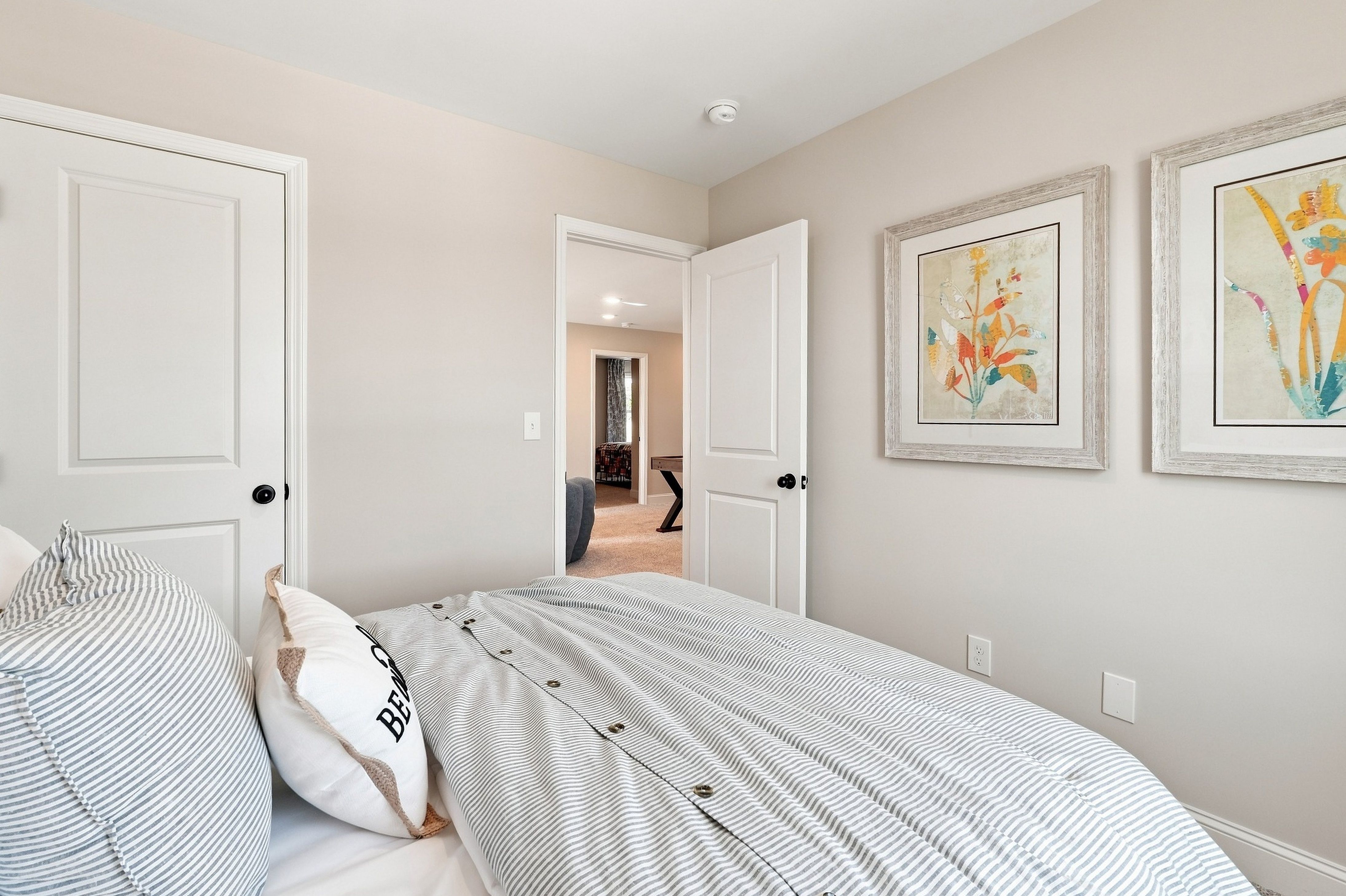 Bright bedroom with striped bedding and framed floral art at Bailey Park by Davidson Homes in Fayetteville, Tennessee