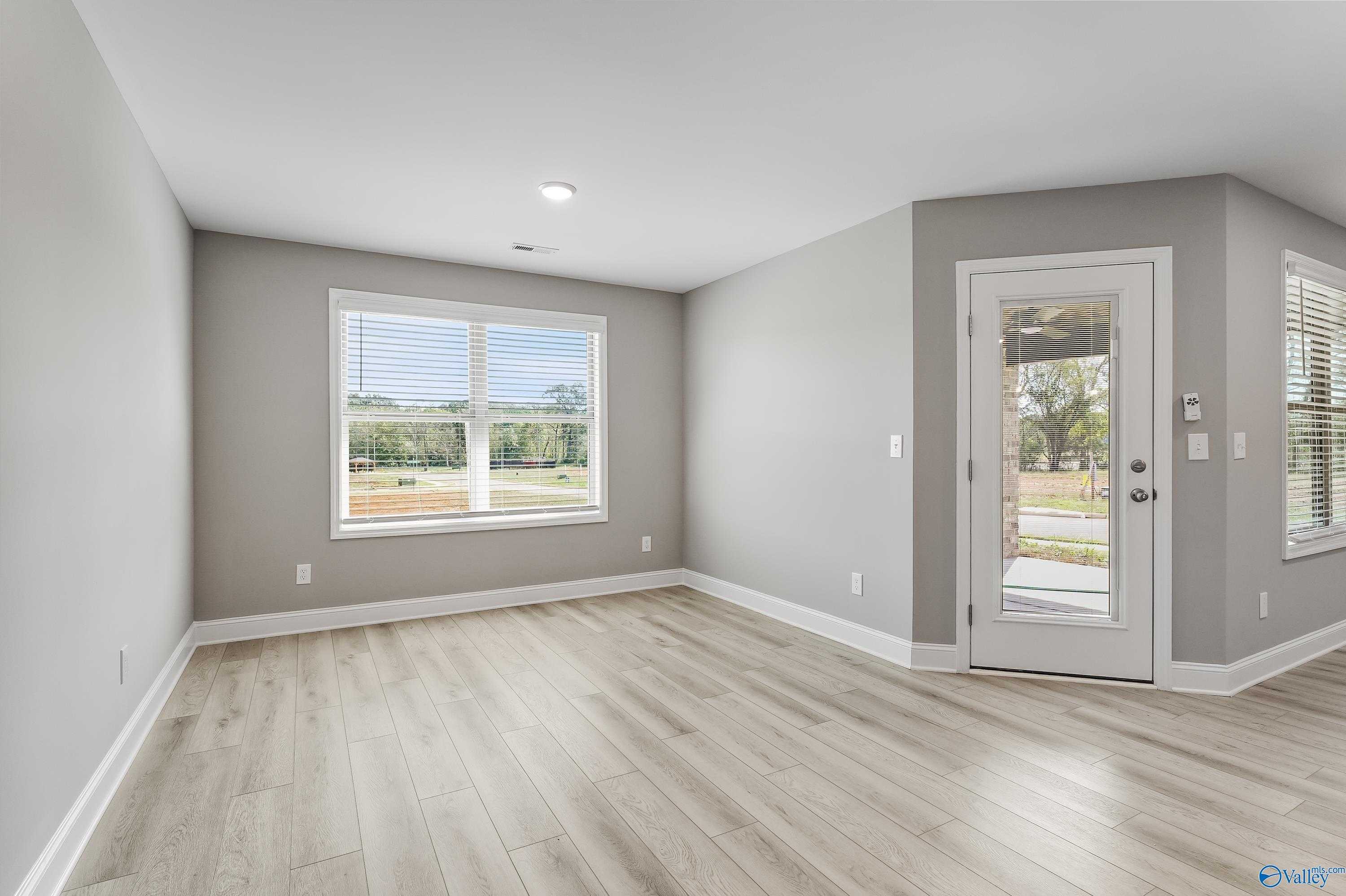 Bright living room with light gray walls, large windows, blinds, and French doors to outdoor patio in The Everett B home, Athens, Alabama