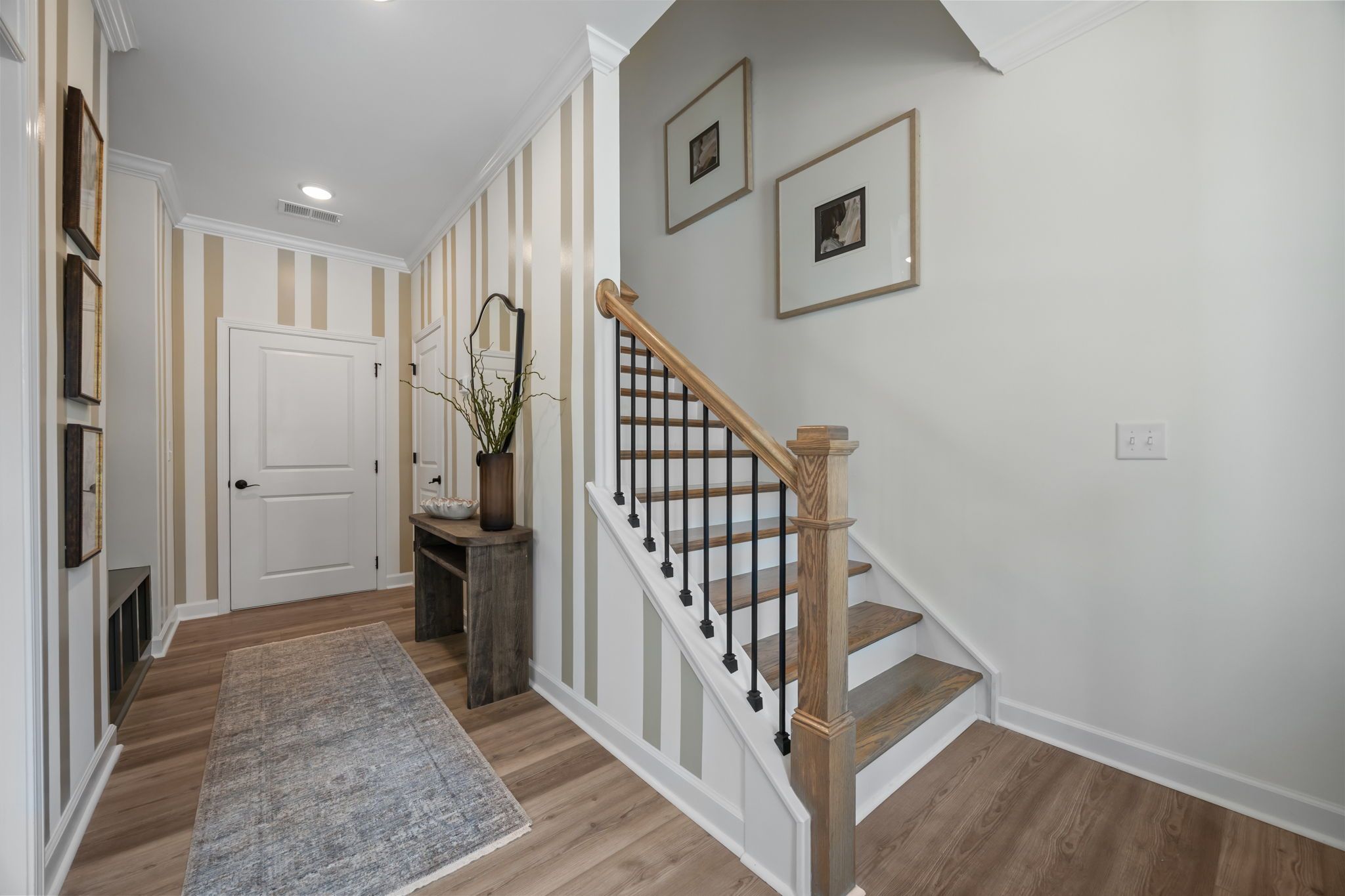 Spacious foyer with striped wallpaper, hardwood floors, framed art, and oak staircase at Camden Park in Knightdale, NC by Davidson Homes