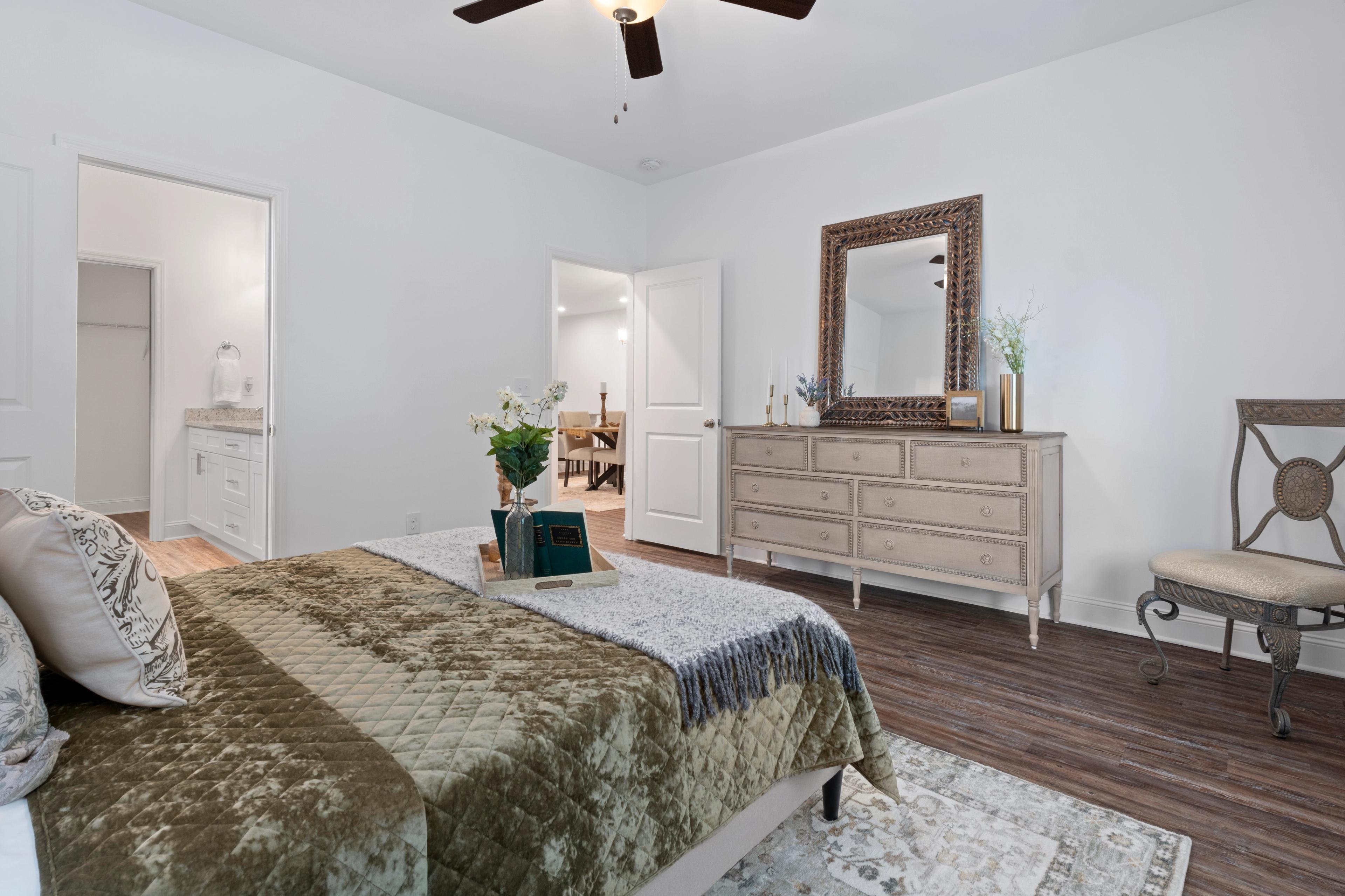 Spacious master bedroom in The Cumberland: tufted king bed with book and throw, antique dresser with mirror, upholstered chair, en-suite bath