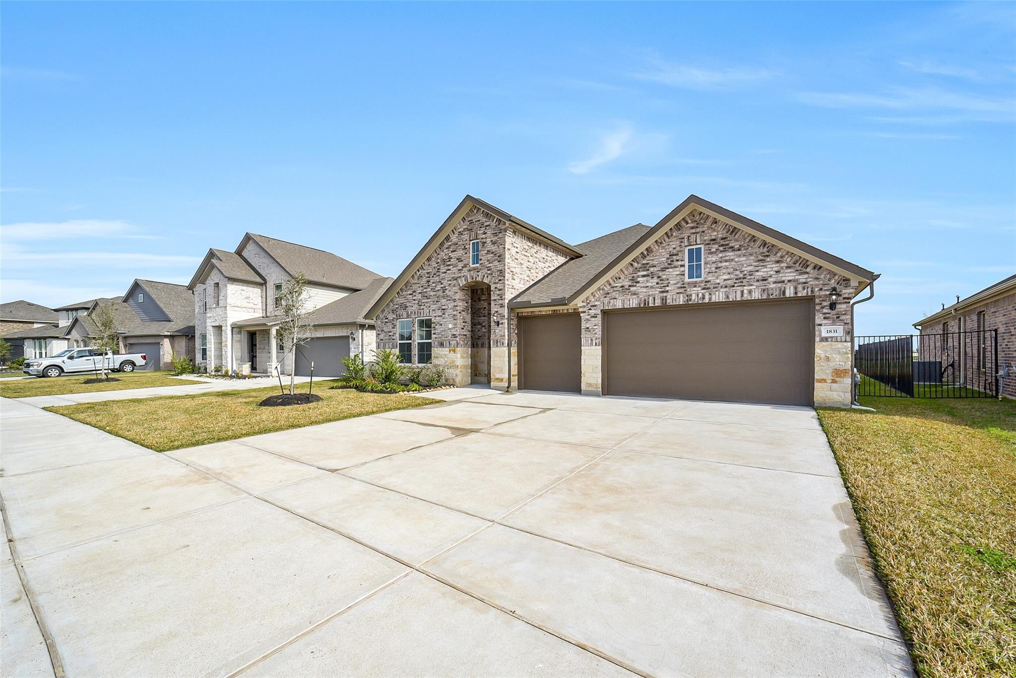 Modern 1-story tan brick home with 3-car garage, wide driveway, and green lawn in Sierra Vista, Rosharon, Texas - Davidson Homes The George B