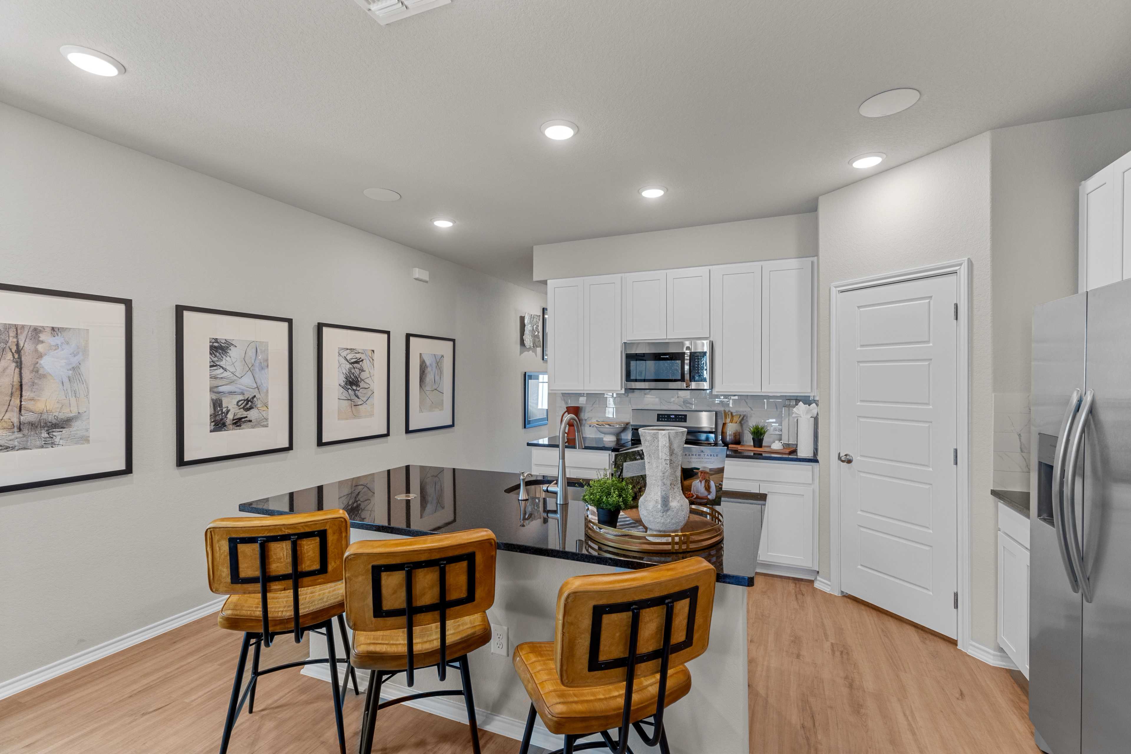 Modern kitchen with black granite island, white cabinets, orange bar stools, and hardwood floors at Applewhite Meadows in San Antonio TX