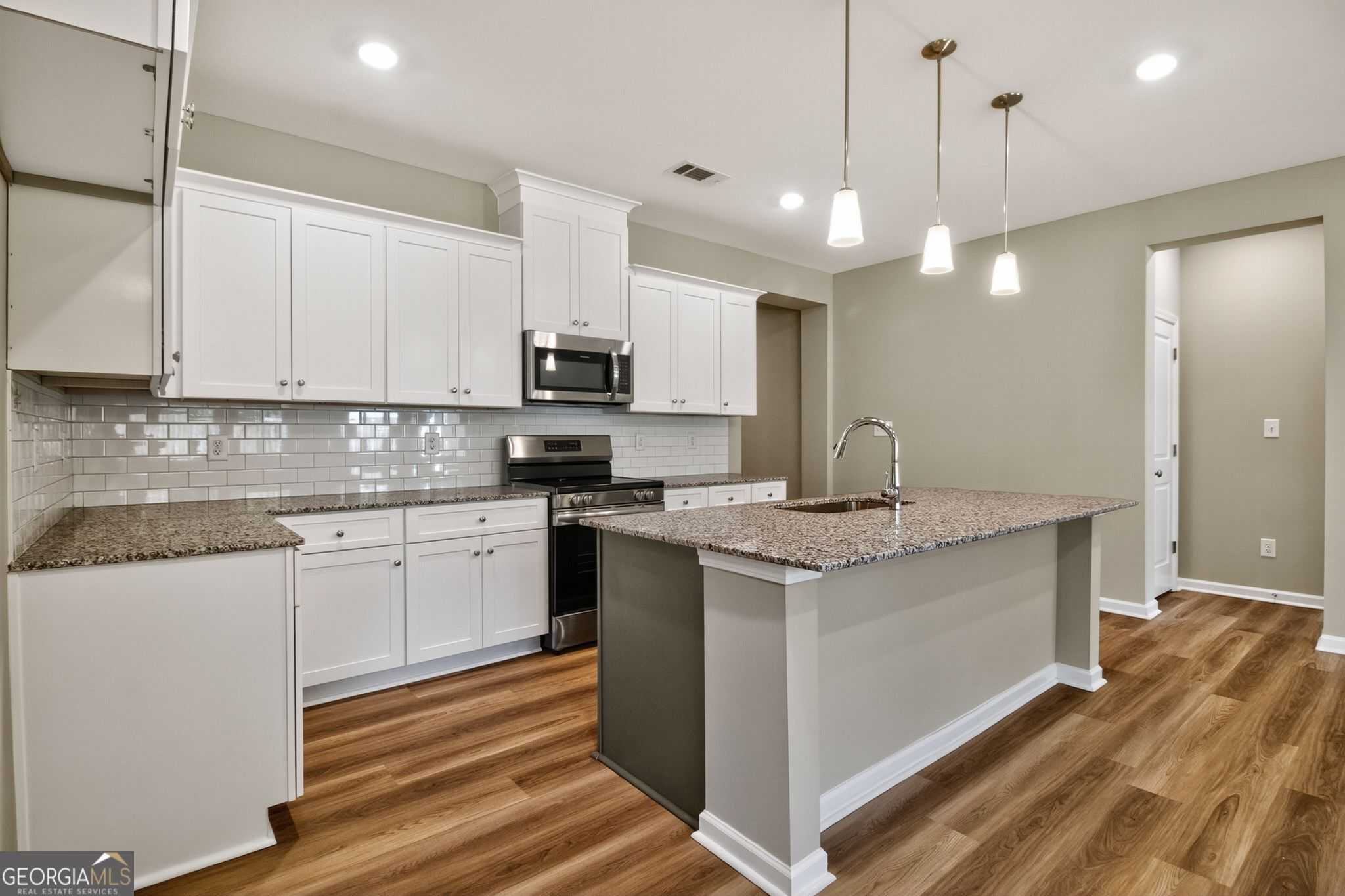 Modern kitchen featuring white cabinets, granite island, subway tile backsplash, stainless appliances in The Luna home by Evermore Homes, Perry, GA