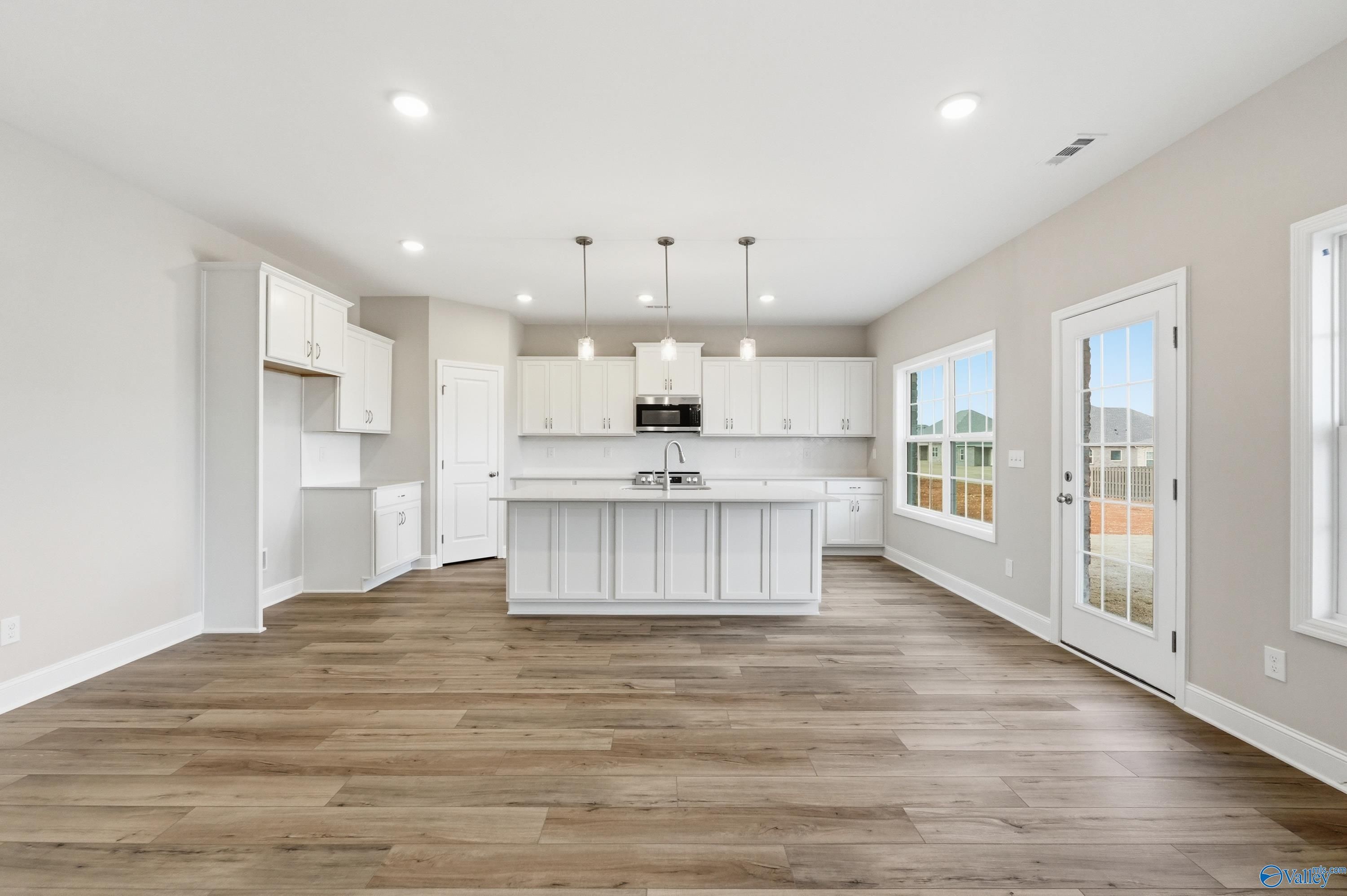 Modern white kitchen with oversized island, stainless appliances, and luxury vinyl plank floors in Davidson Homes The Madison A, Meridianville, AL