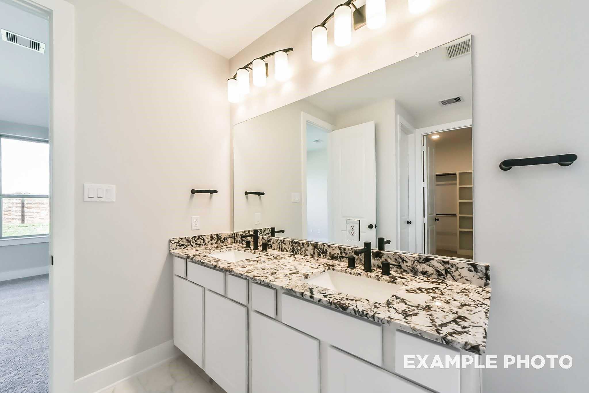 Luxurious master bathroom double vanity with granite countertop, white cabinets, and sconce lighting in Davidson Homes The Philip C, Rosharon, Texas