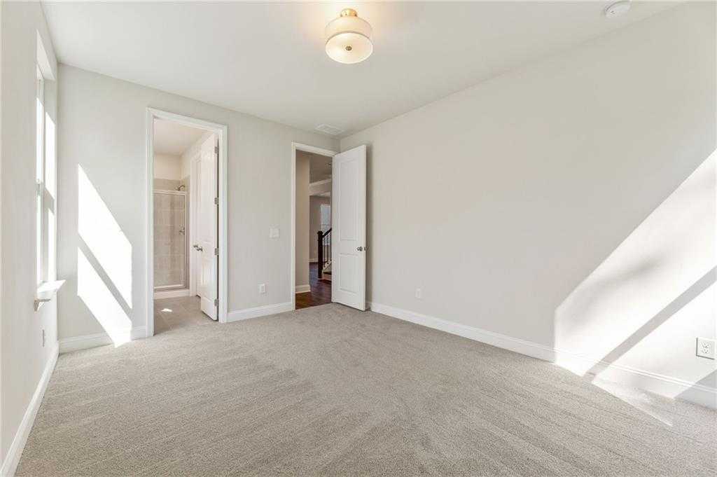 Sunlit bedroom with attached bathroom door and neutral carpet in Davidson Homes The Danbury E, Buford, Georgia
