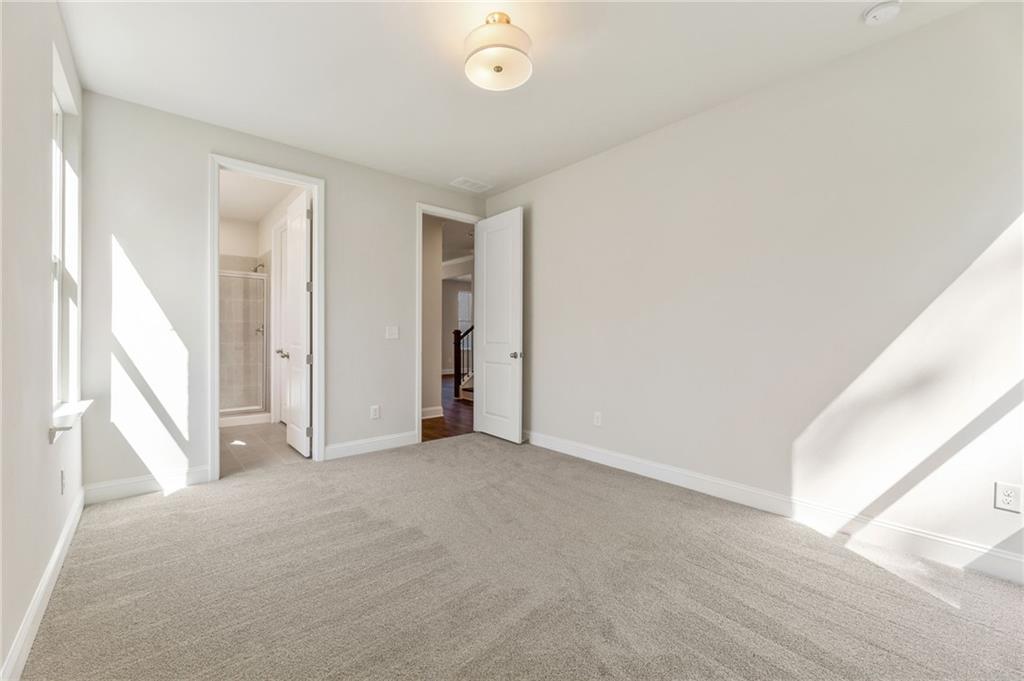 Sunlit secondary bedroom with neutral walls, carpeted floor, en-suite bath access in Davidson Homes The Danbury E, Buford, GA