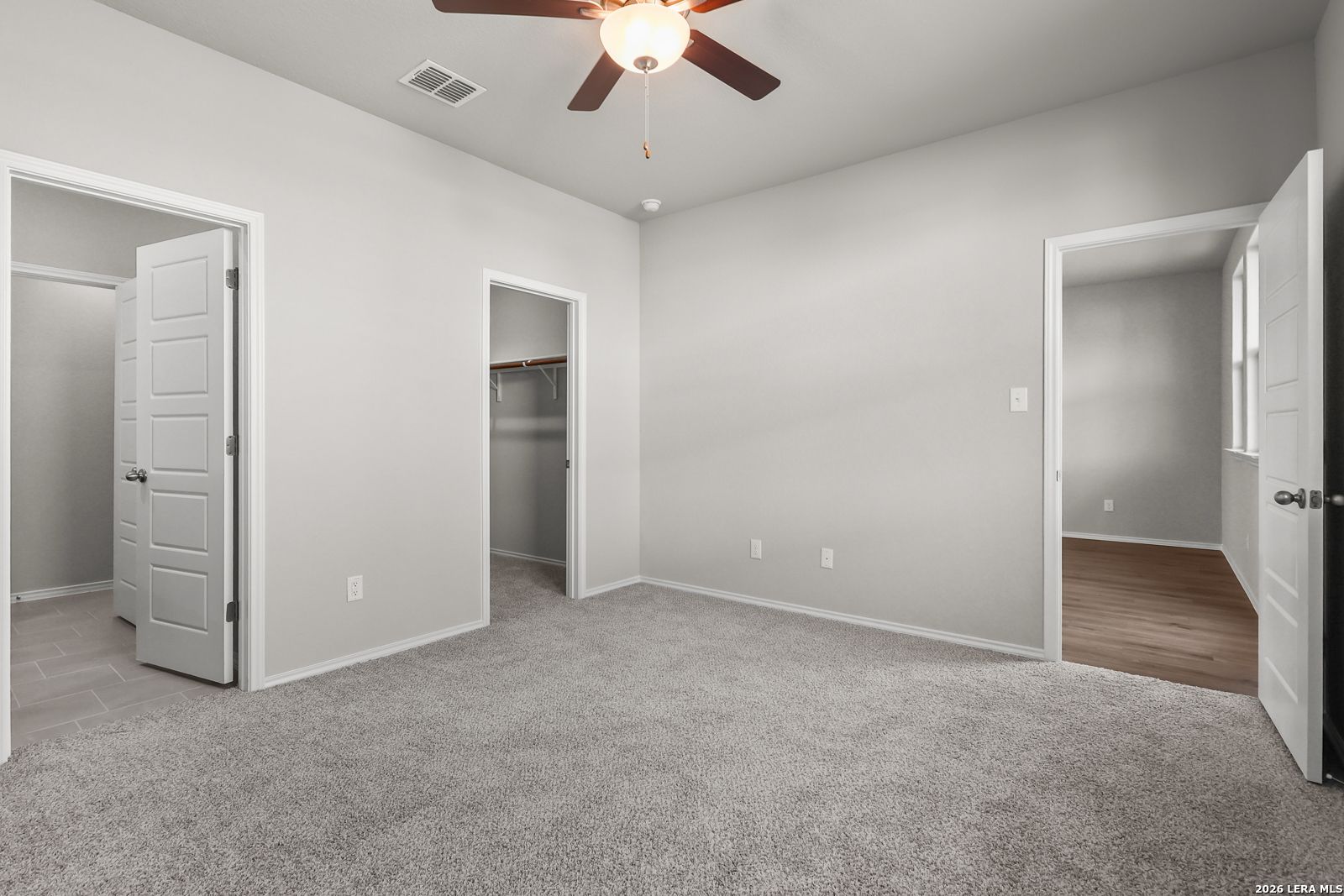 Spacious bedroom with gray carpet, ceiling fan, and walk-in closets in Davidson Homes The Frio B, San Antonio, Texas