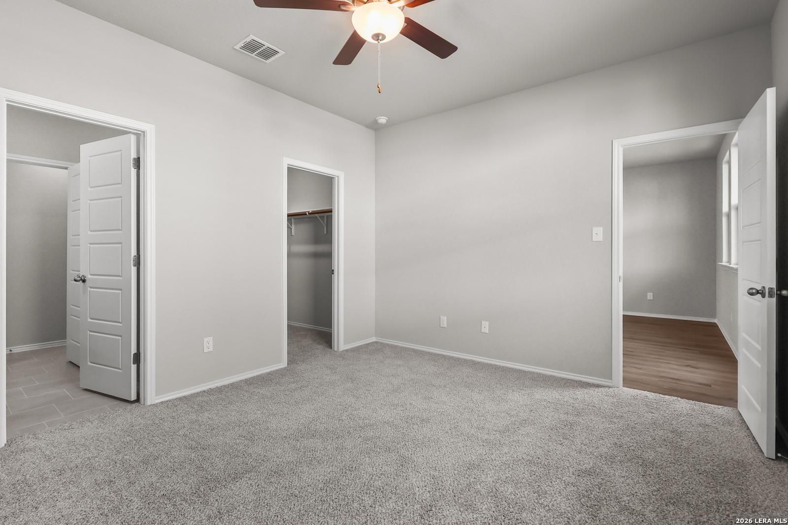 Spacious bedroom with gray carpet, ceiling fan, and walk-in closets in Davidson Homes The Frio B, San Antonio, Texas