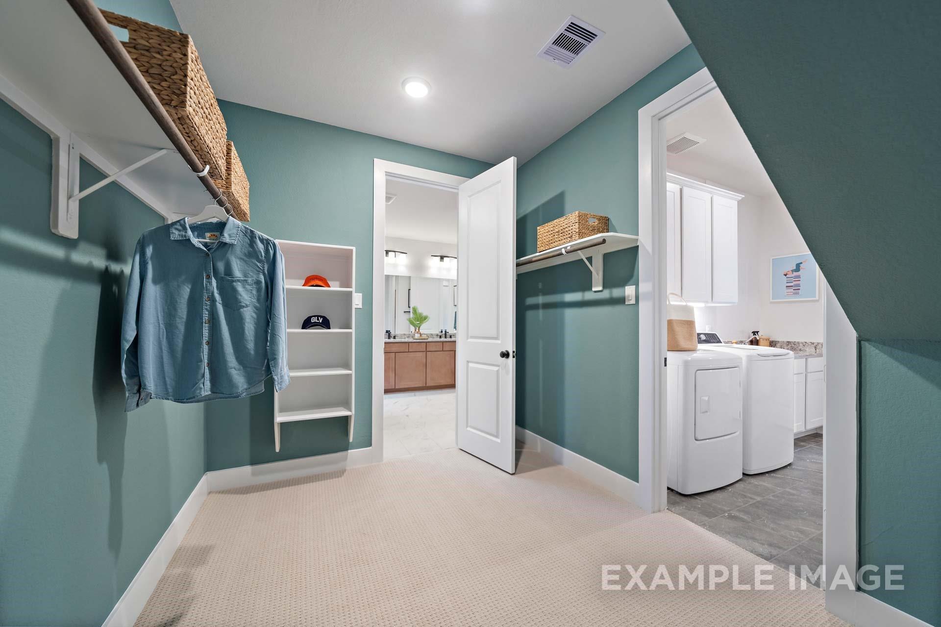Spacious teal laundry room with built-in shelves, wicker baskets, washer-dryer, and adjacent bathroom in Davidson Homes The Edward A, Texas City