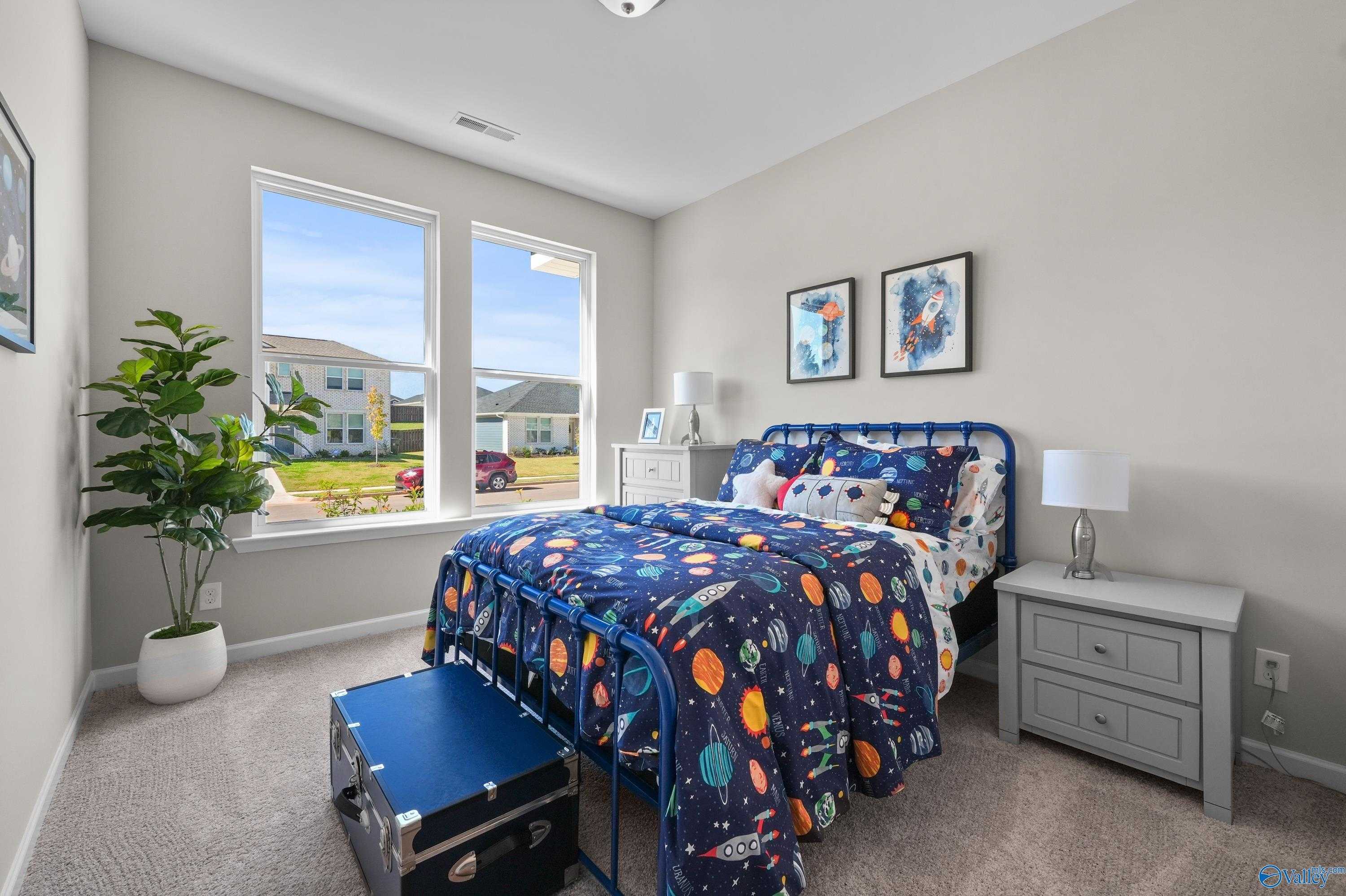 Cozy child's bedroom with space-themed bedding, large windows, and potted plant in The Malibu floor plan by Evermore Homes, Madison, Alabama
