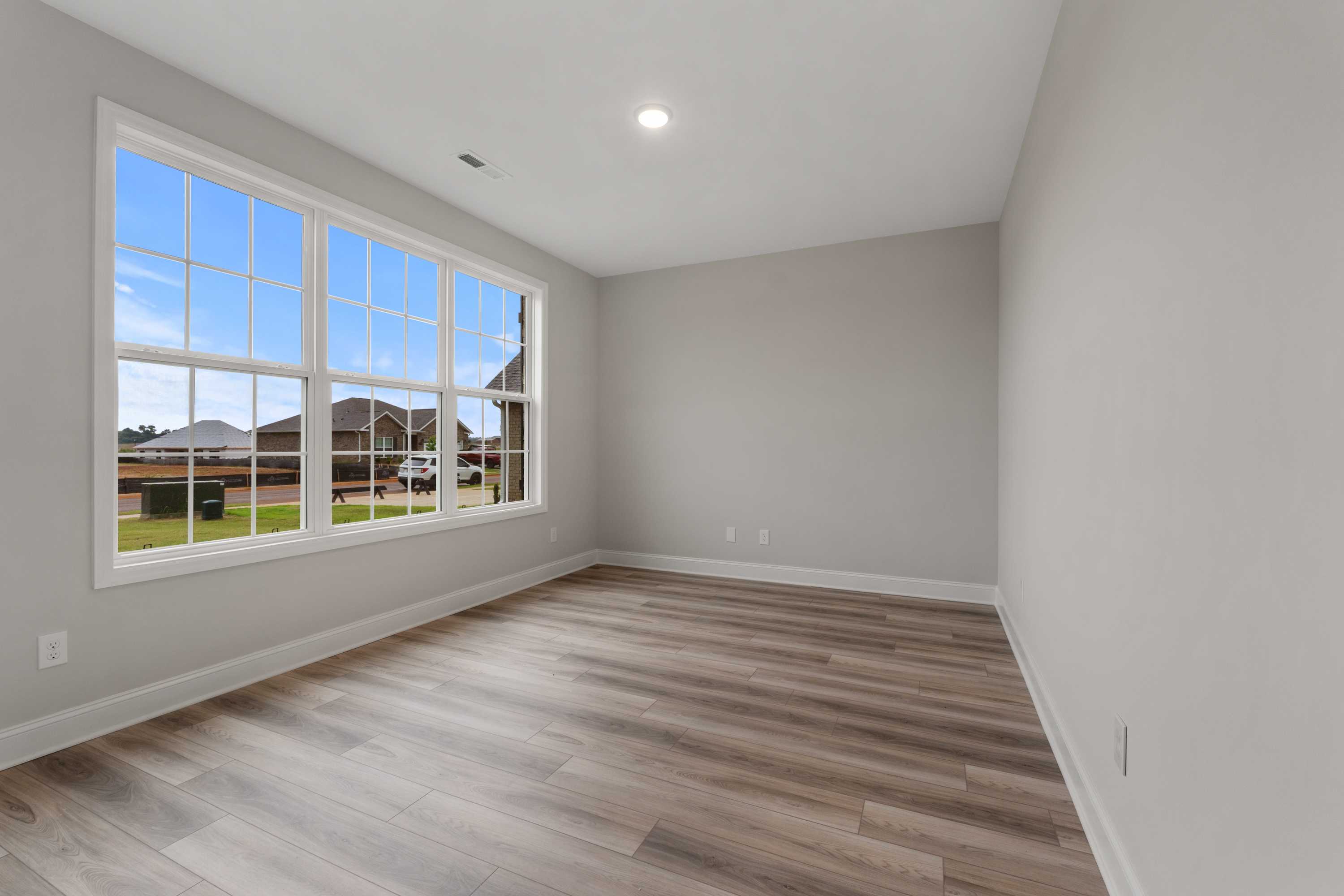 Bright secondary bedroom in The Oxford Davidson Homes design with large triple windows, gray walls, and hardwood floors