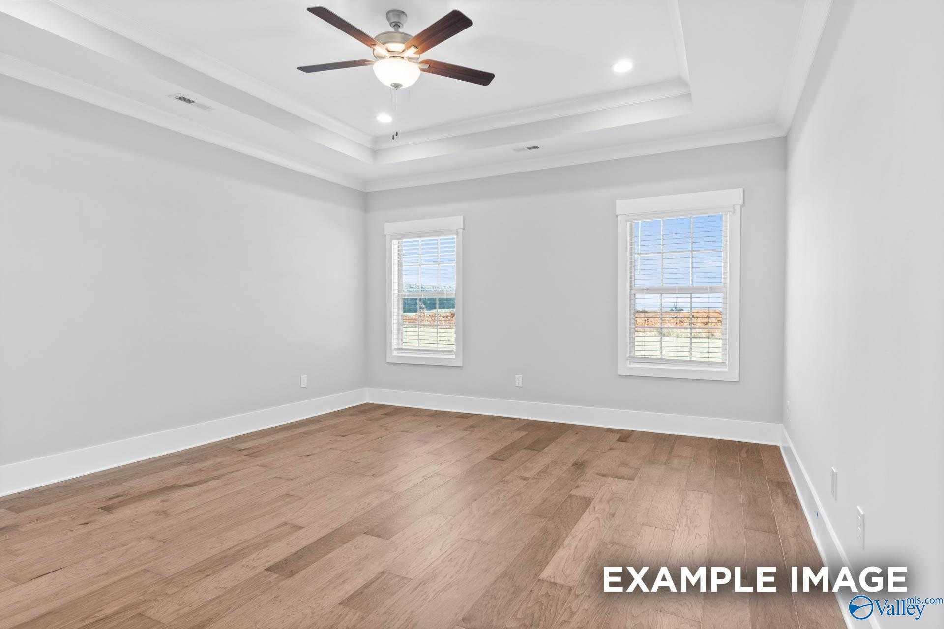 Spacious bedroom with light gray walls, hardwood floors, ceiling fan, and large windows in Davidson Homes The Rockford, Meridianville, Alabama