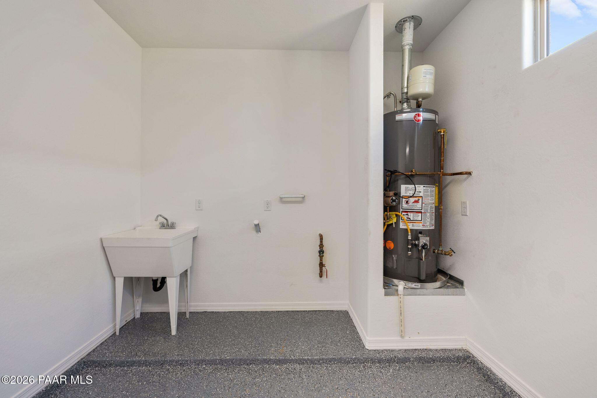 White utility laundry room with pedestal sink, Rheem water heater, and epoxy floor in Davidson Homes The Frontier A, Prescott Valley, AZ