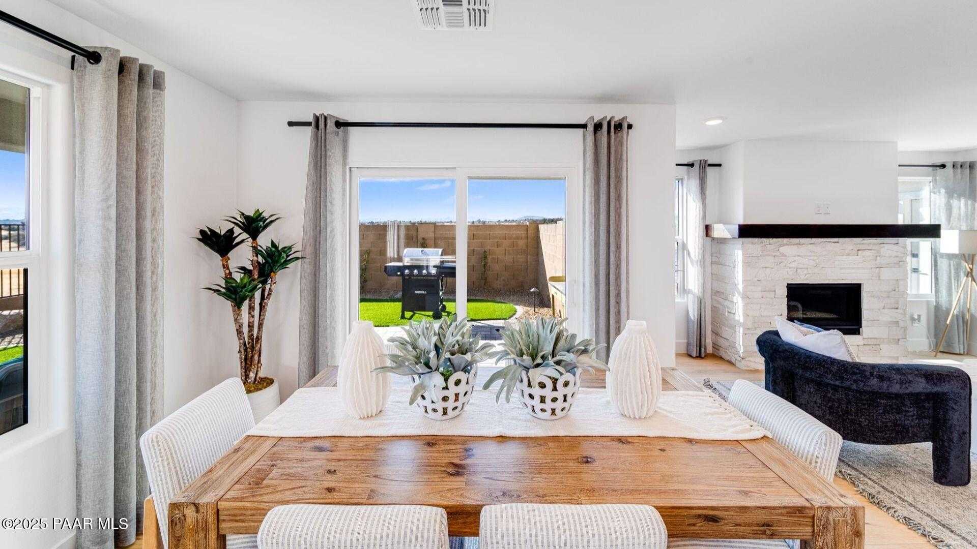 Elegant dining room with wooden table, white chairs, potted plants, and fireplace overlooking green backyard in Prescott, AZ home