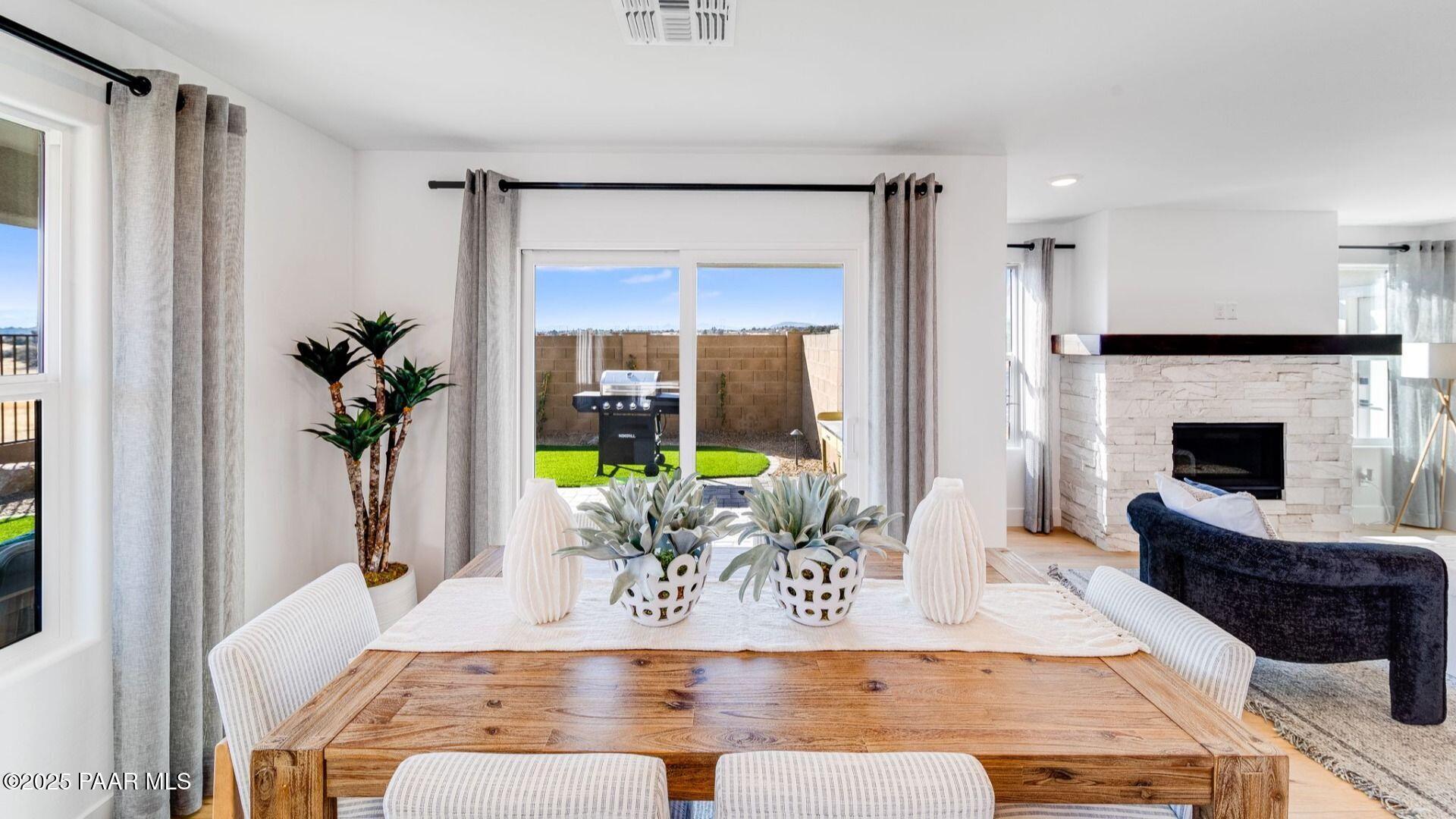 Elegant dining room with wooden table, white chairs, potted plants, and fireplace overlooking green backyard in Prescott, AZ home