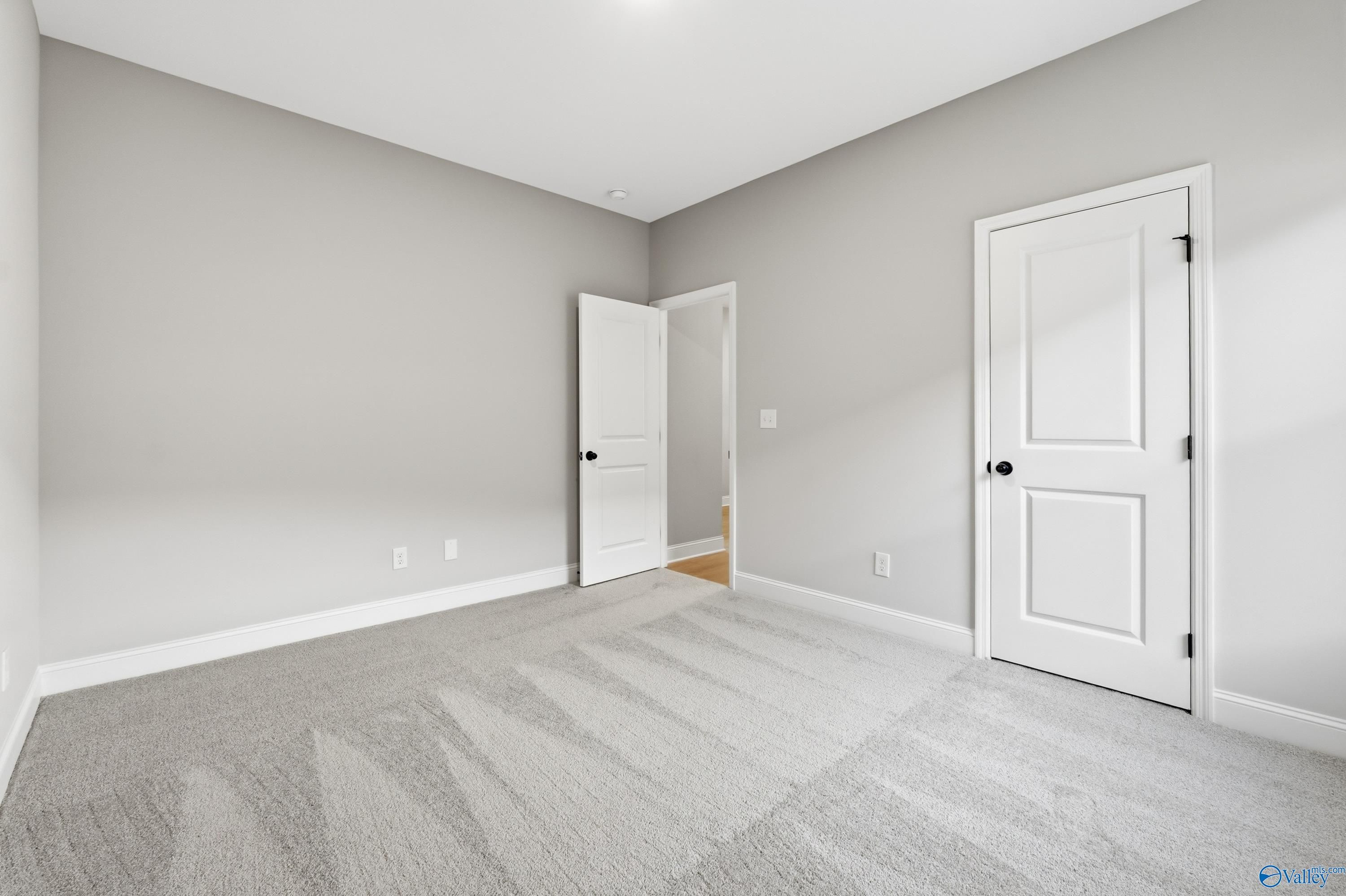 Empty secondary bedroom featuring light gray walls, white doors, and plush carpet in Davidson Homes The Daphne C, Athens, Alabama