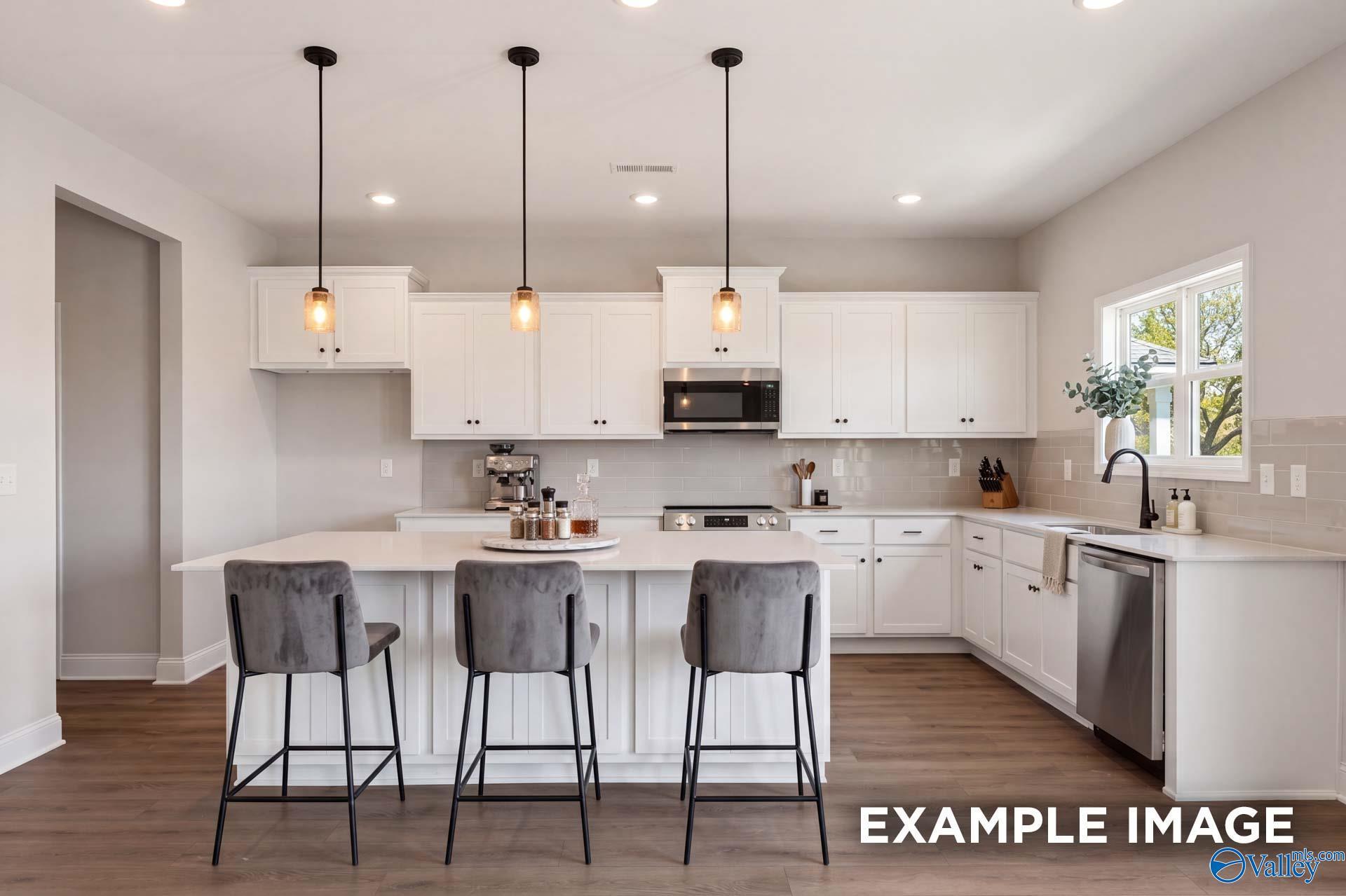 Modern white kitchen with island, pendant lighting, and stainless steel appliances in The Chelsea D home, Cullman, Alabama.