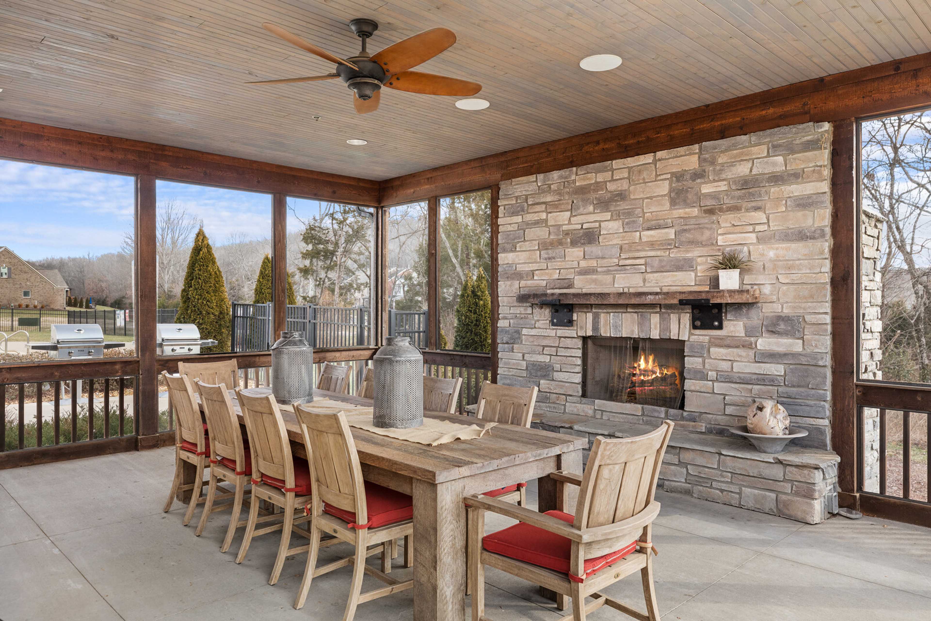 Screened porch with rustic wooden dining table, red chairs, stone fireplace, ceiling fan at Carellton in Gallatin TN