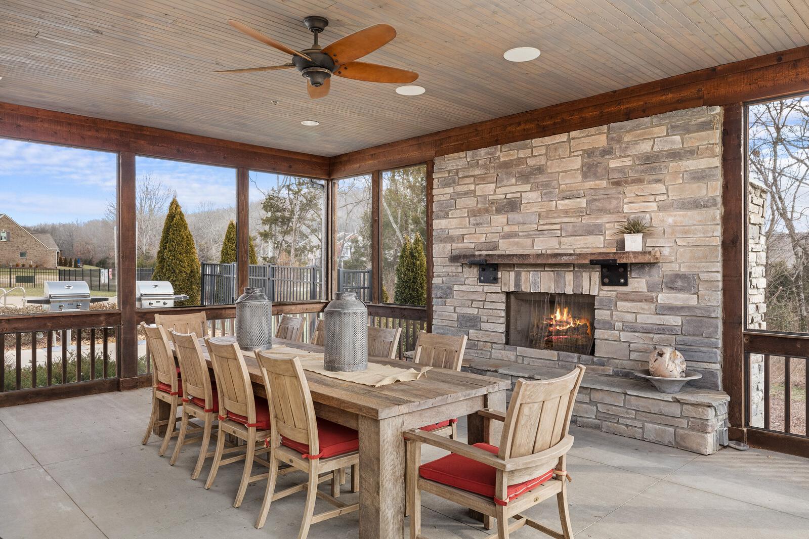 Screened porch with rustic wooden dining table, red chairs, stone fireplace, ceiling fan at Carellton in Gallatin TN