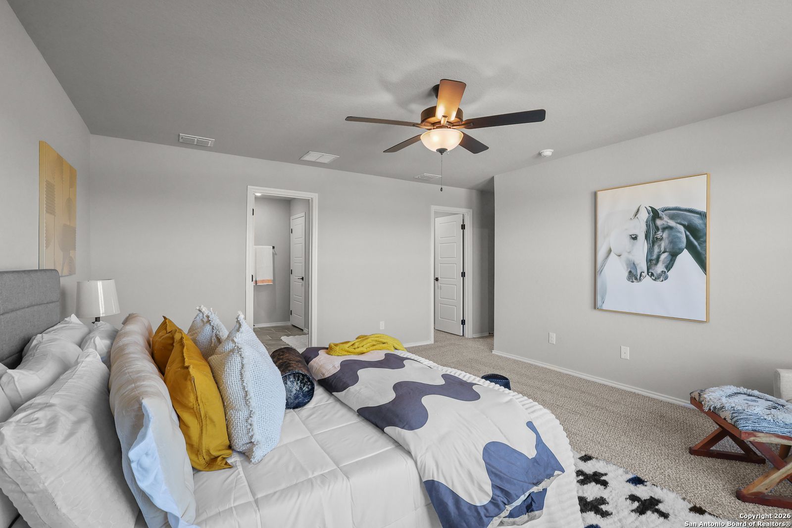 Cozy bedroom with queen bed, colorful pillows, ceiling fan, and horse wall art in Davidson Homes The Murray K, San Antonio