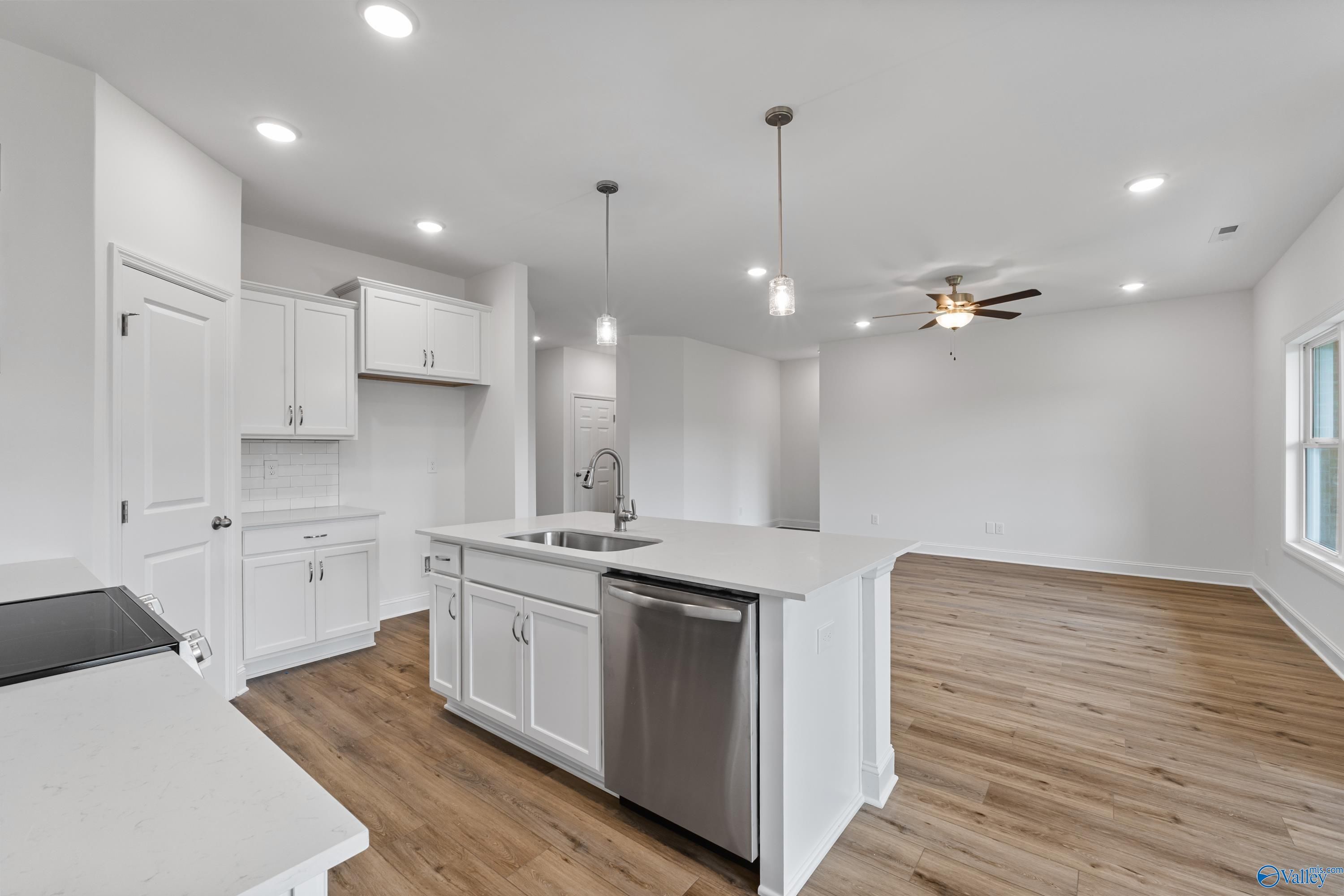 Modern open-concept kitchen with white cabinets, quartz island, stainless sink and dishwasher in The Asheville C, New Market, AL