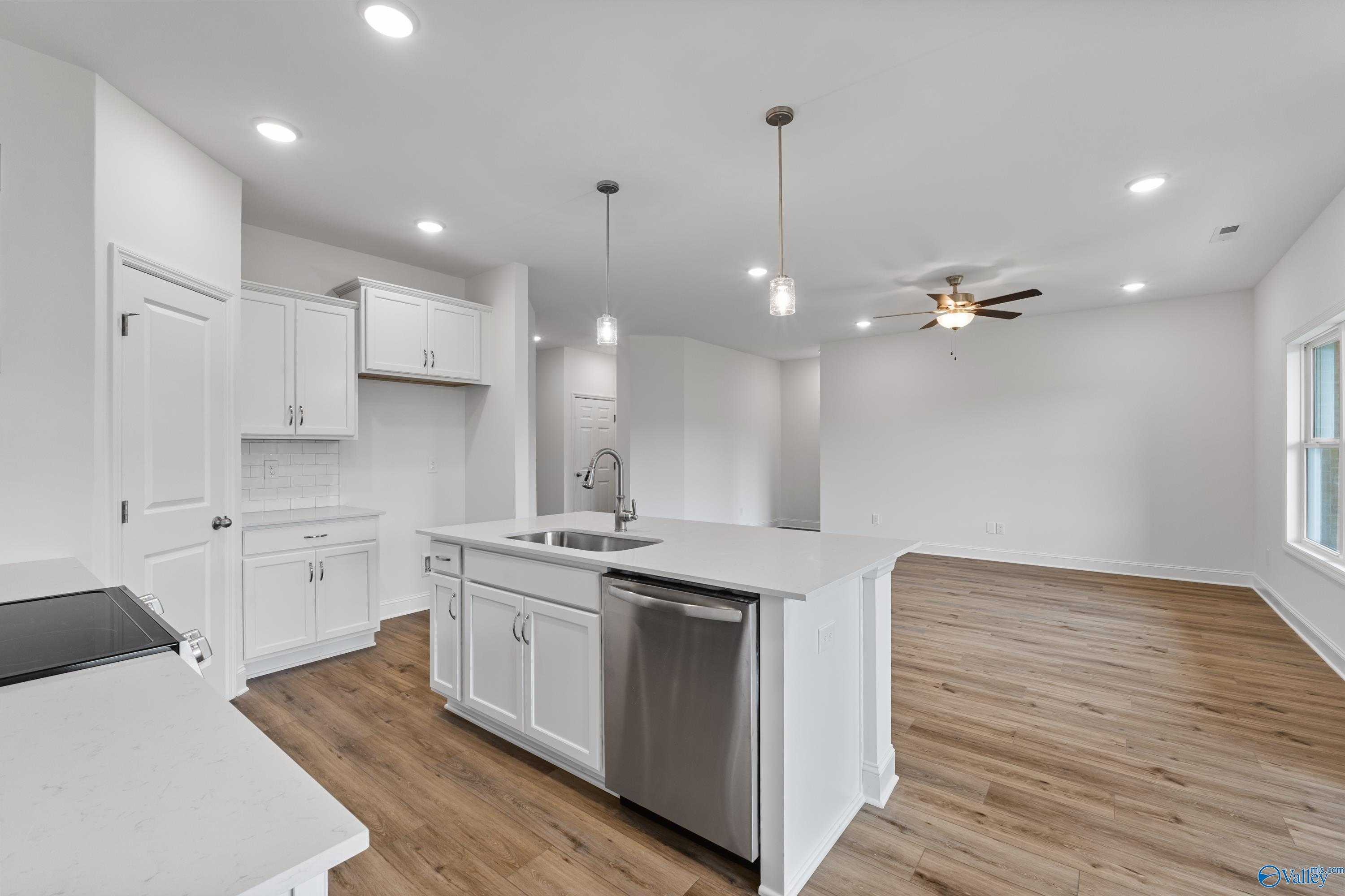 Modern open-concept kitchen with white cabinets, quartz island, stainless sink and dishwasher in The Asheville C, New Market, AL
