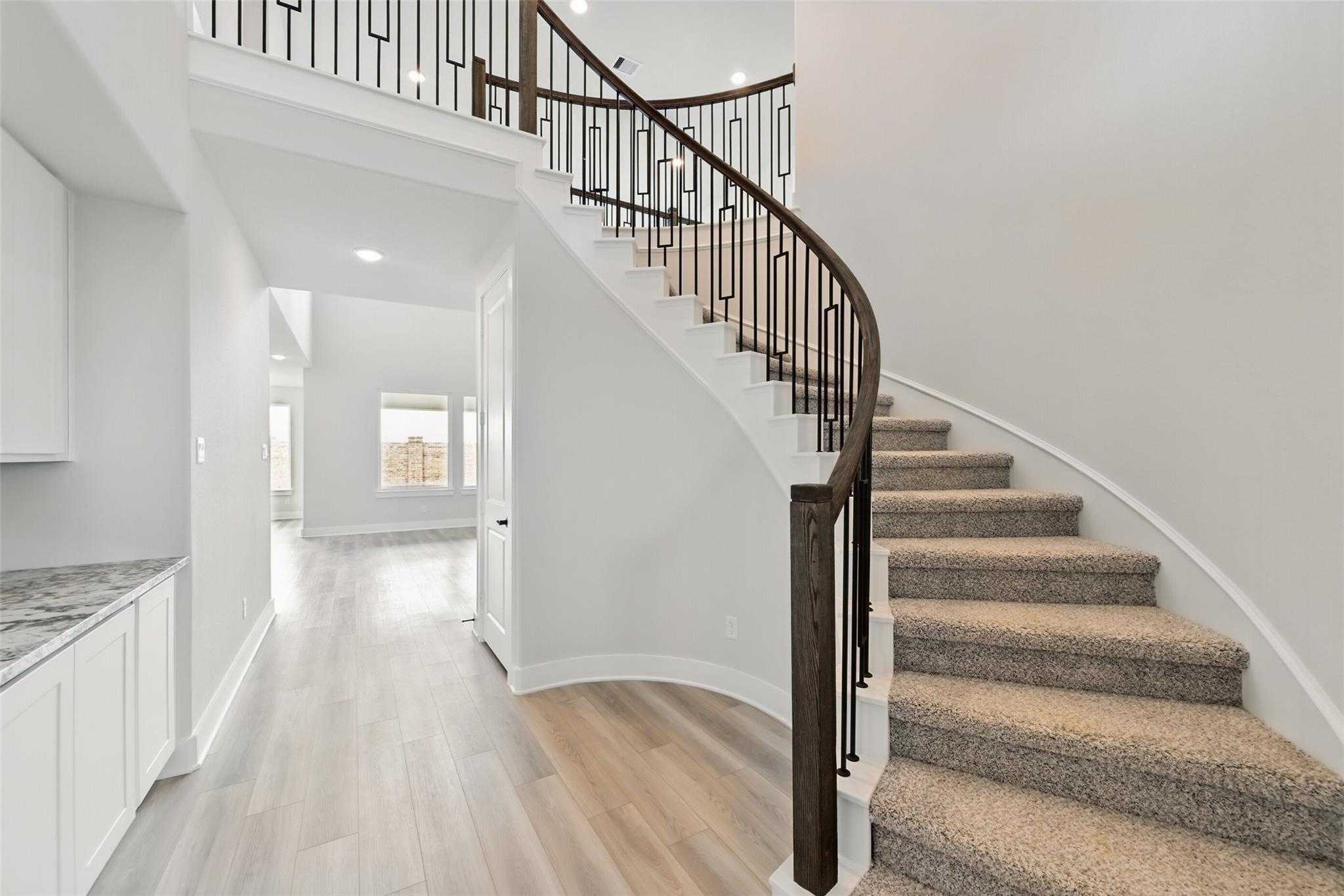 Elegant curved staircase with wrought iron railings in bright foyer of Davidson Homes The Victoria C in Lago Mar, Texas City