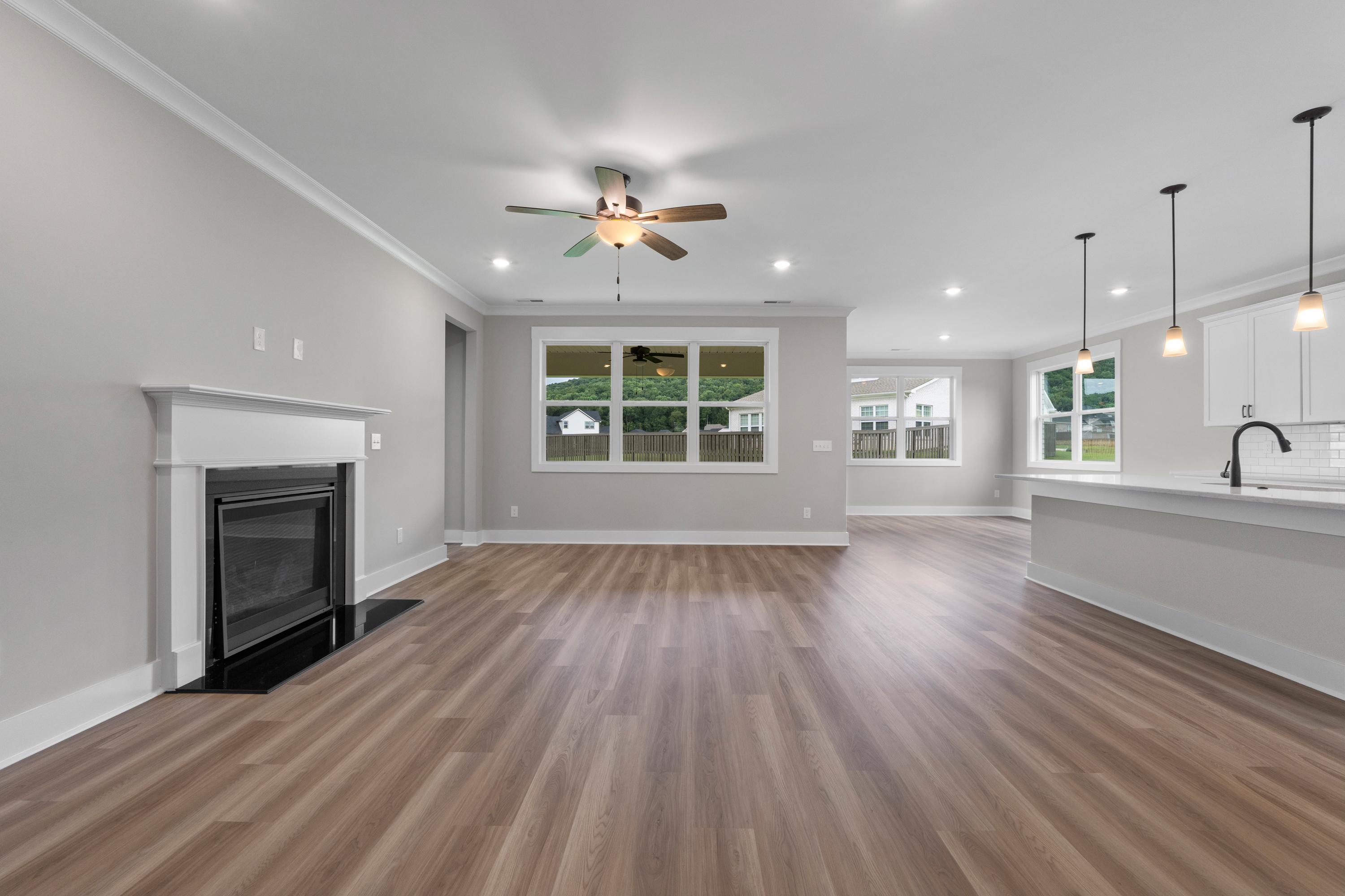 Spacious open-concept living room and kitchen in The Oxford home design, with wood floors, white fireplace, and large windows